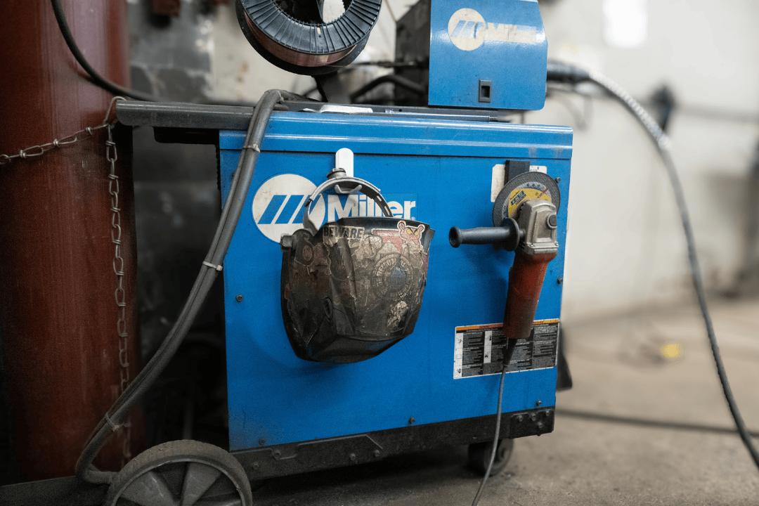 Gator magnetic hooks hold a welding helmet and angle grinder on a blue Miller welding machine.