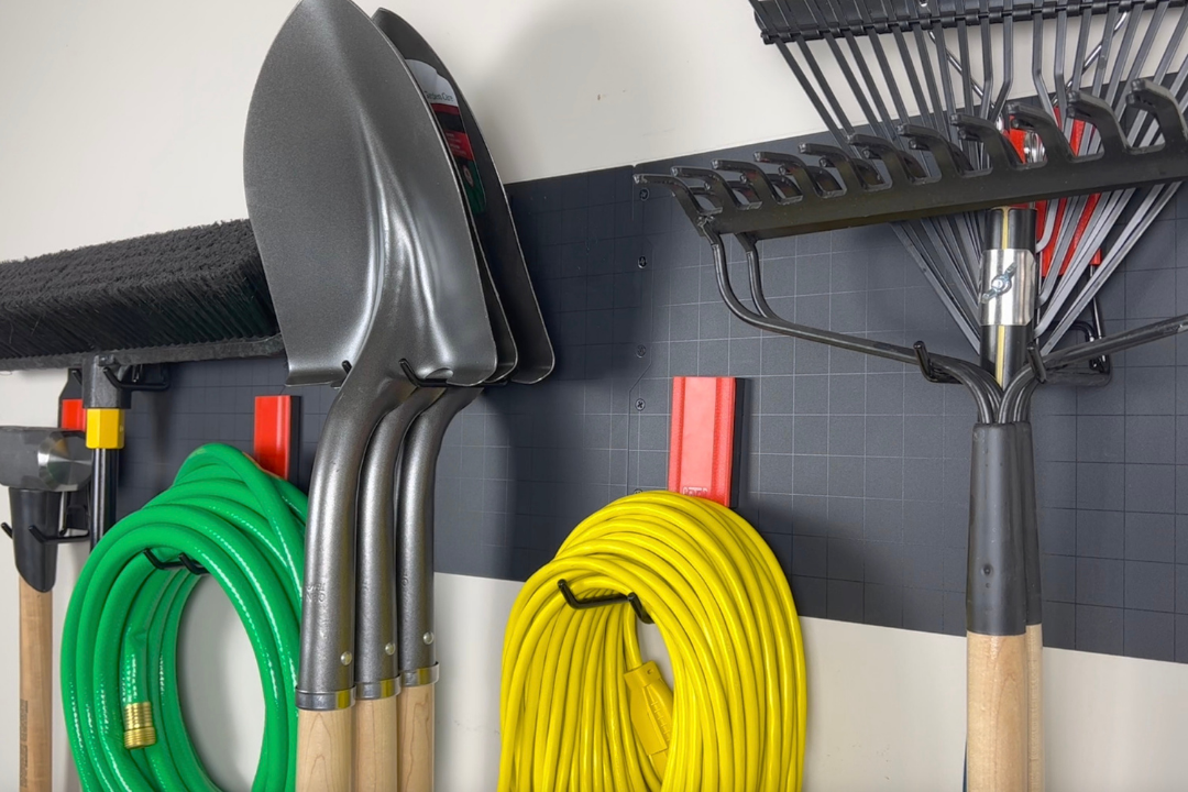 Red Gator magnetic hooks hold three shovels, a garden hose and extension cord on a steel garage wall.