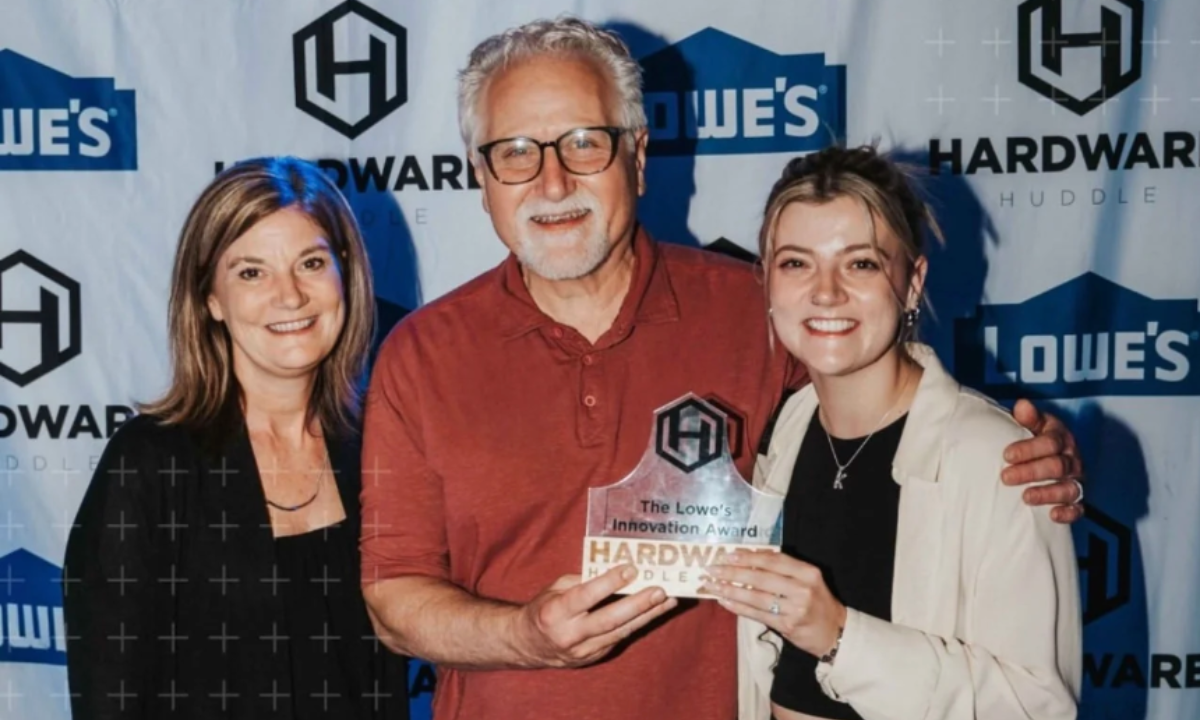 Three people display the Lowe's Innovation Award plaque in front of a Lowe's Hardware Huddle backdrop.