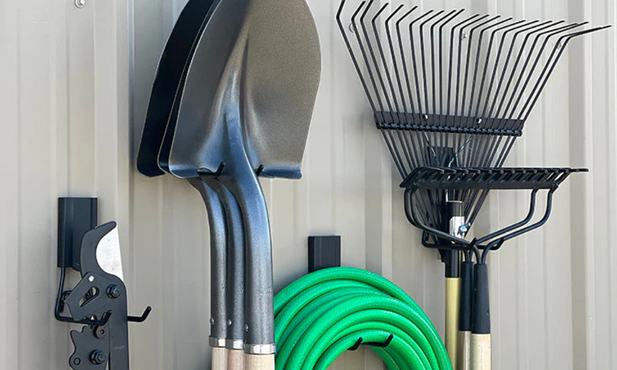 Red Gator magnetic hooks store shovels, rake and coiled garden hose on a steel pole barn wall.