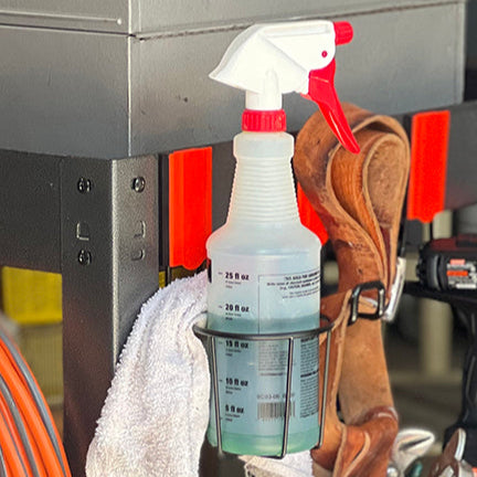 The black Gator Cup Holder with a red lever is shown holding a spray bottle, demonstrating its versatility. This cup holder provides secure storage for cleaning supplies or beverages and attaches easily to steel surfaces, making it a practical addition to any workspace.