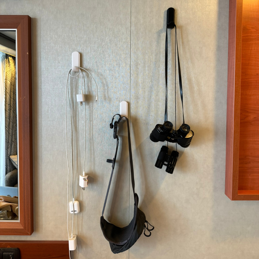 White and black magnetic hooks mounted in a cruise cabin holding charging cables, a small bag, and binoculars, providing versatile storage and organization for travel or small spaces.