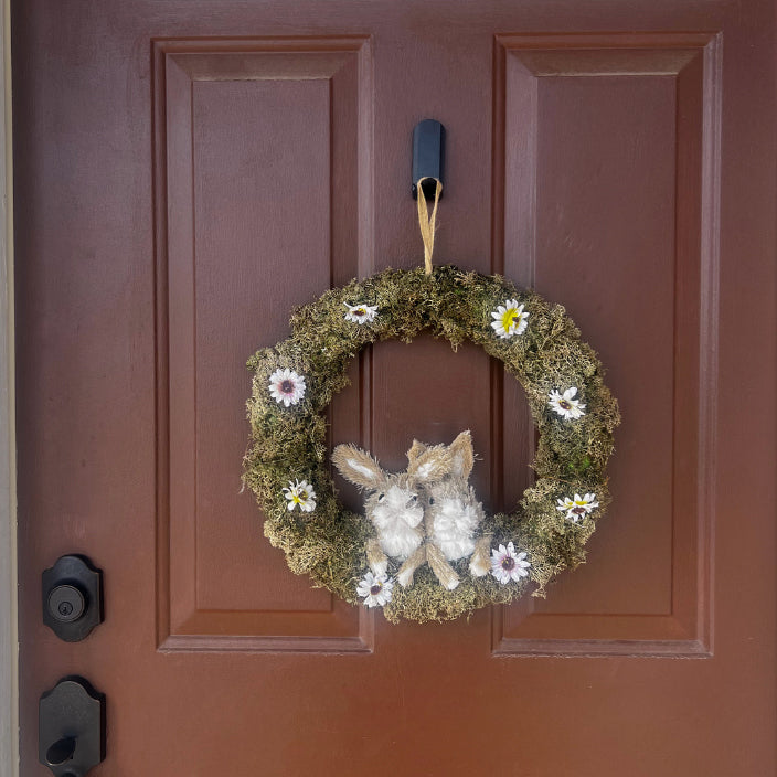 lack magnetic hook on a metal front door holding a decorative spring wreath with faux moss, flowers, and two bunny figures, showcasing seasonal home décor hanging solution.