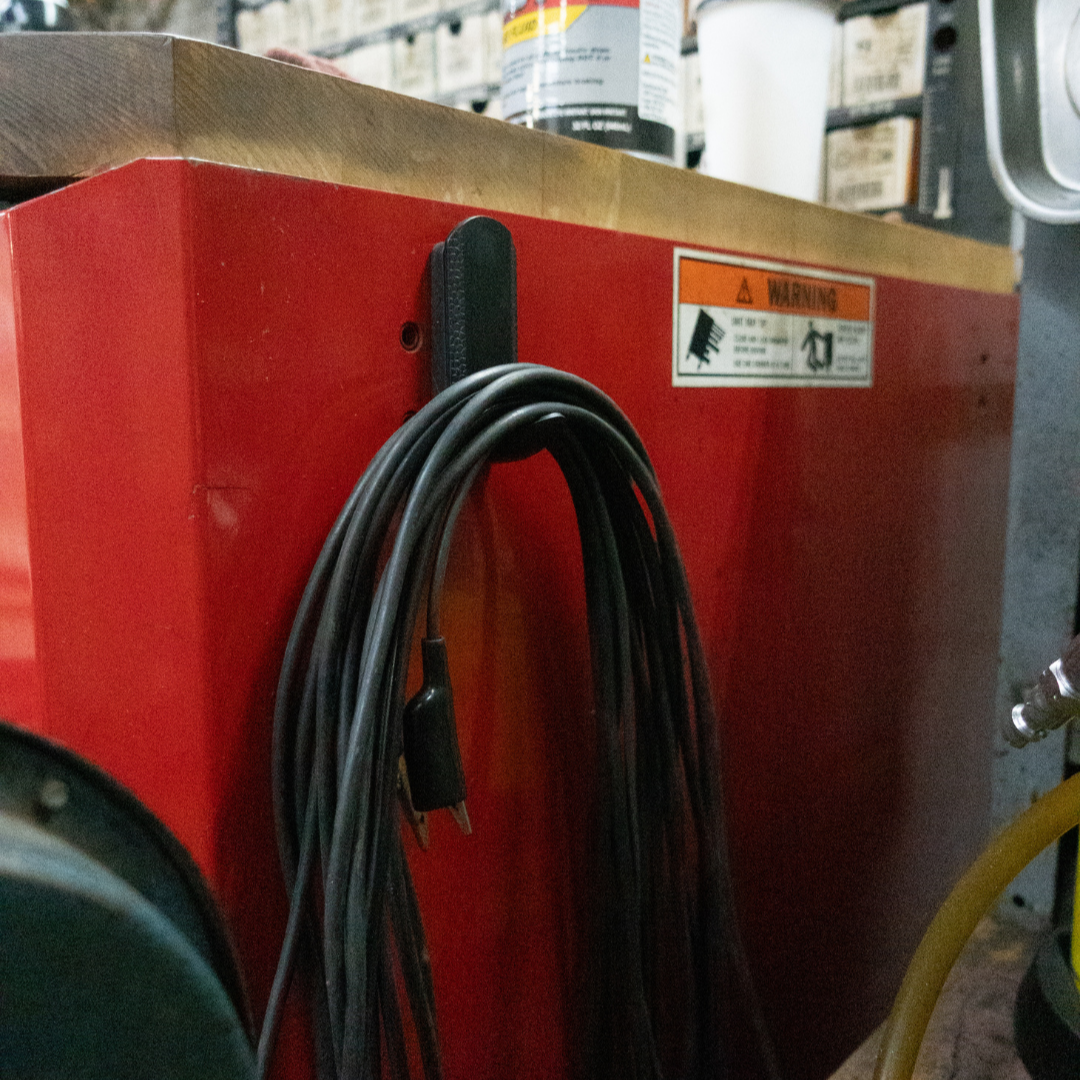 Black magnetic hook mounted on a red steel toolbox holding a coiled extension cord, showcasing heavy-duty garage storage and organization.