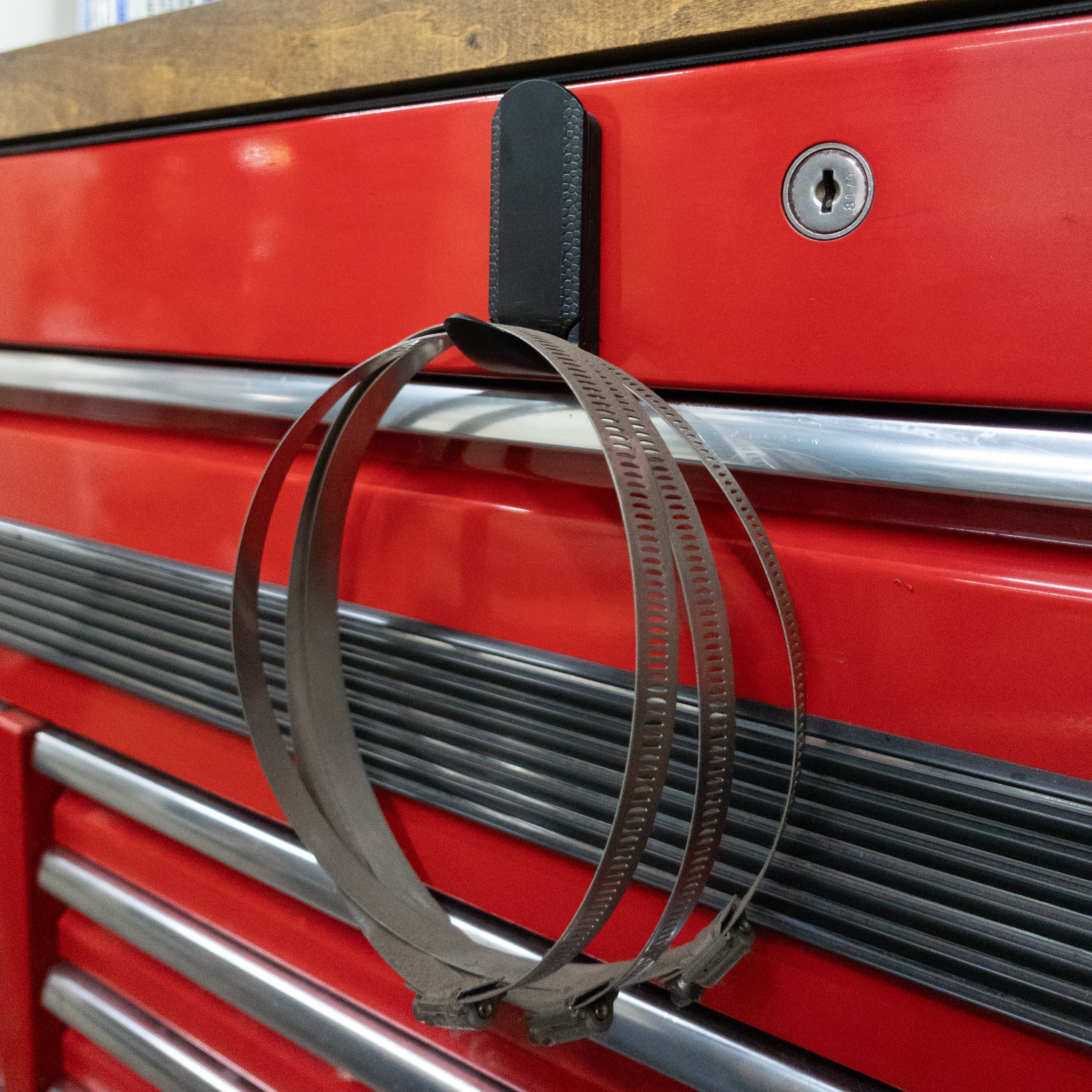 Black magnetic hook attached to a red steel toolbox holding large metal hose clamps, demonstrating durable garage and workshop storage capability.