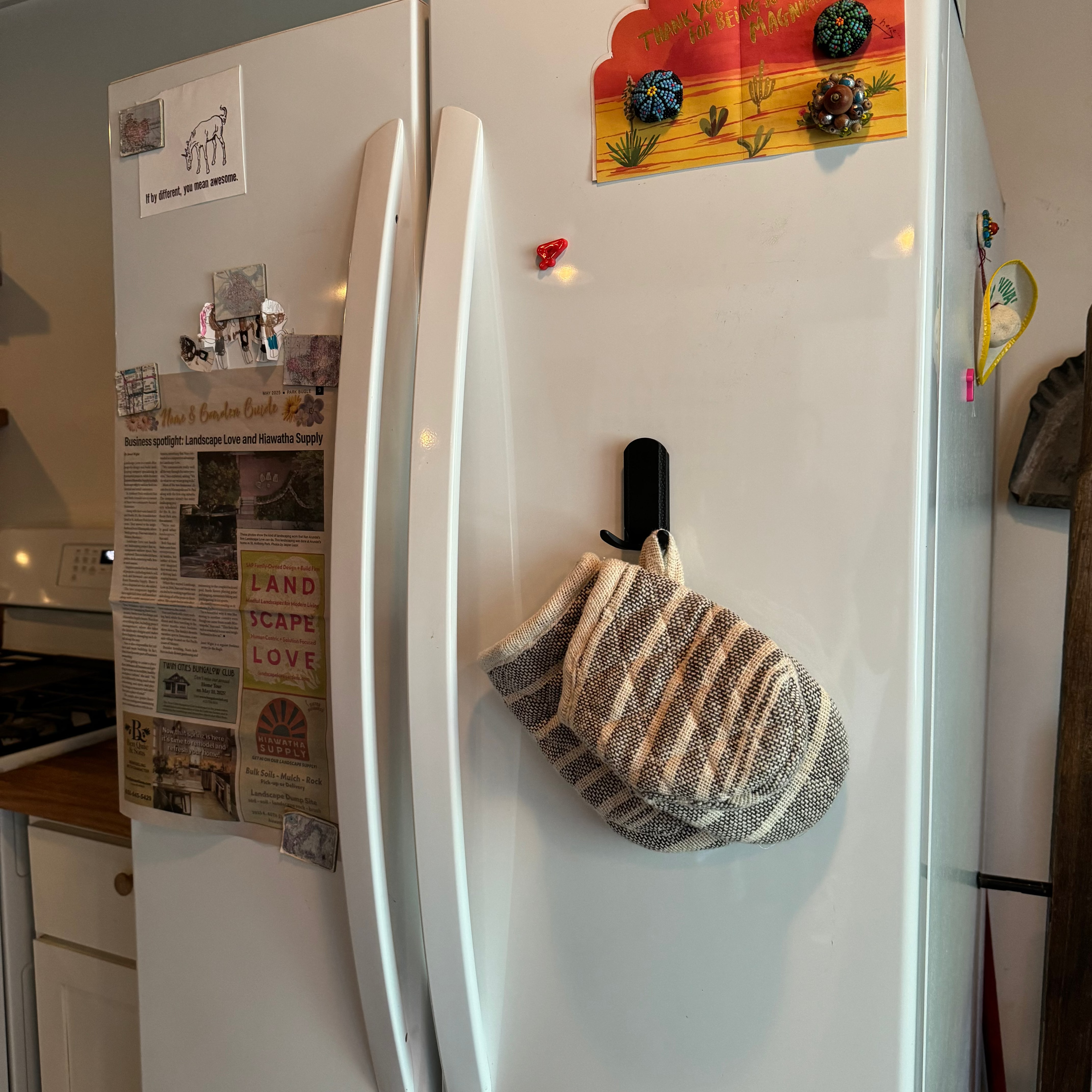 Black magnetic hook on a white refrigerator holding a striped oven mitt, providing a convenient and accessible kitchen storage solution.