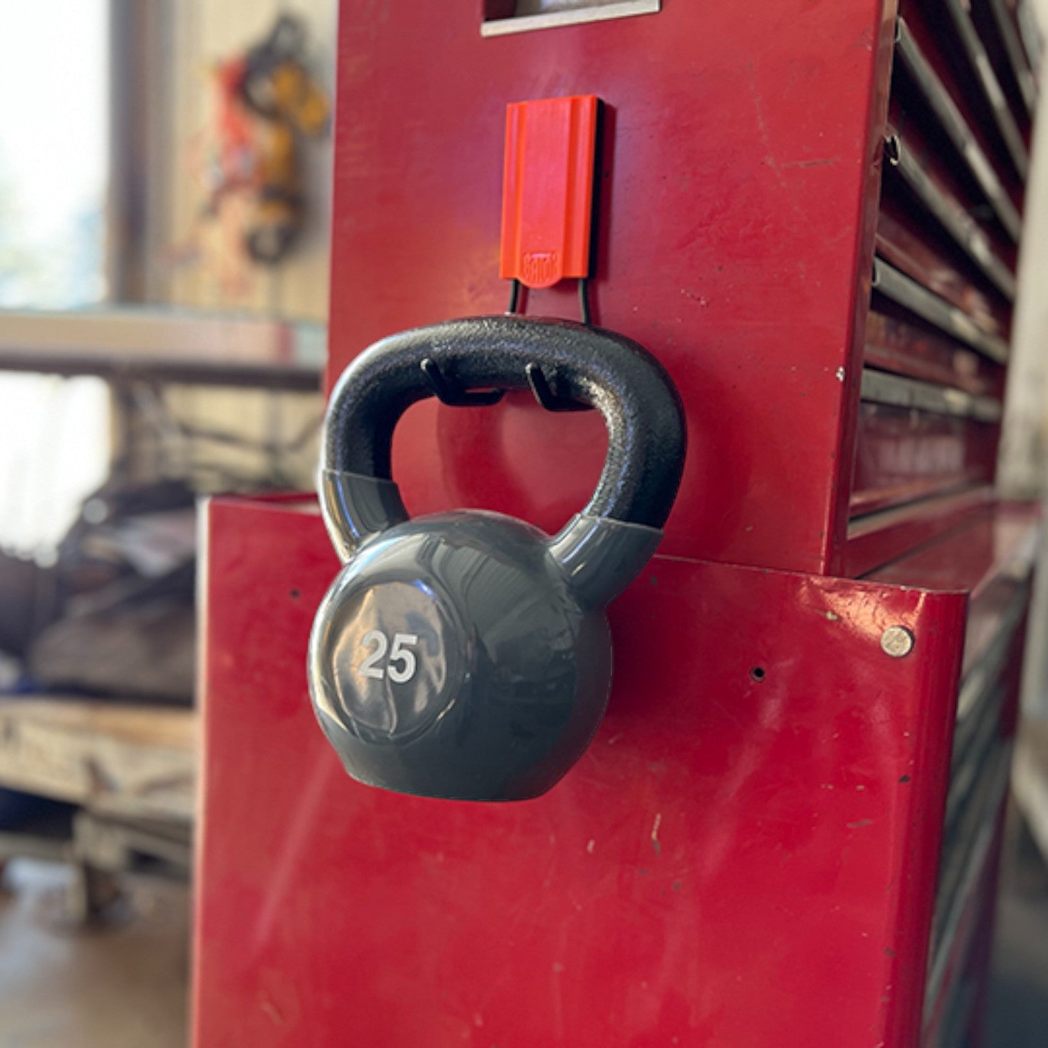A 25-pound kettlebell is suspended from a red Gator Magnetics heavy duty magnetic hook attached to the side of a red steel tool chest.
