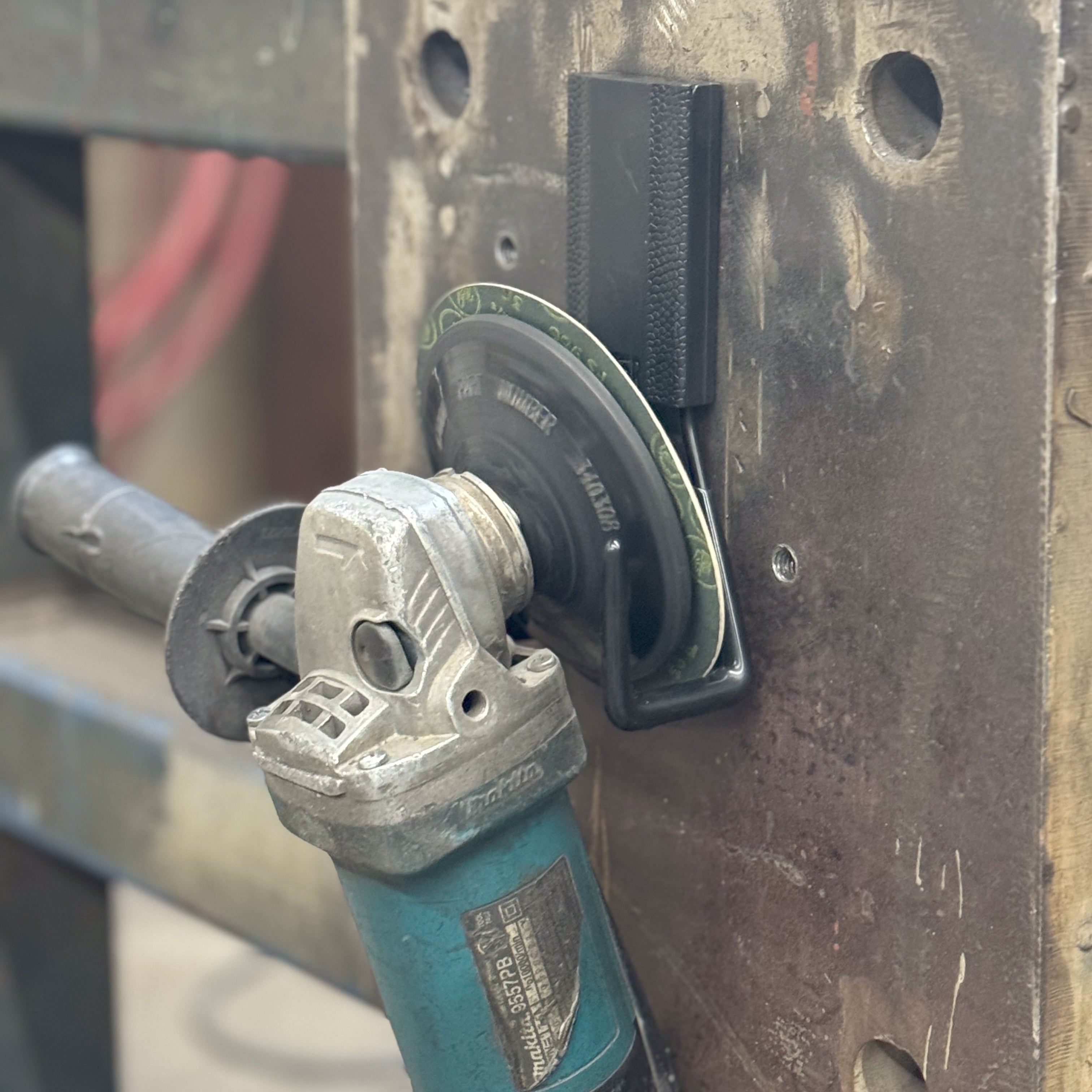 Angle grinder hanging from a red Gator heavy-duty magnetic hook on a steel equipment rack.