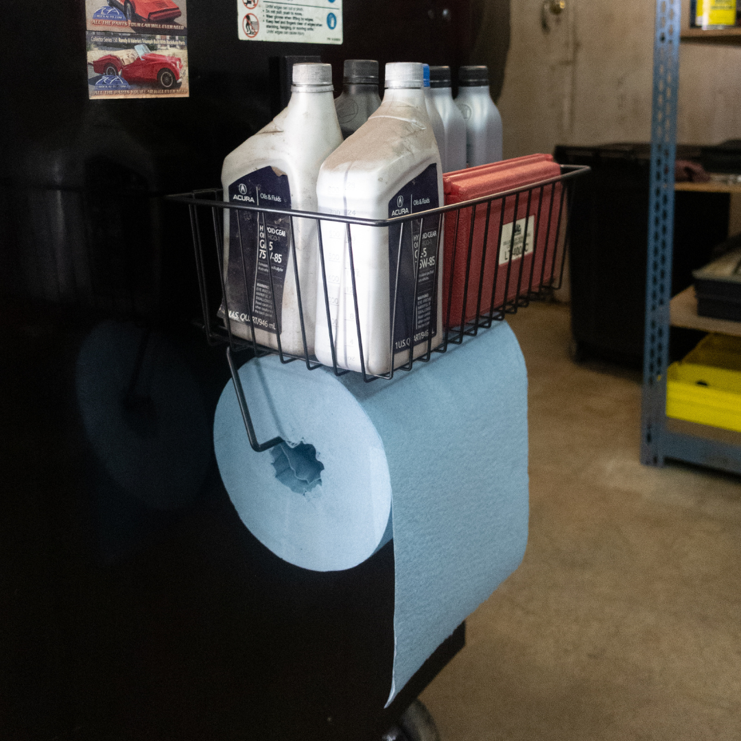 Black Gator magnetic basket with towel bar on a steel toolbox holding automotive fluids and paper towels.