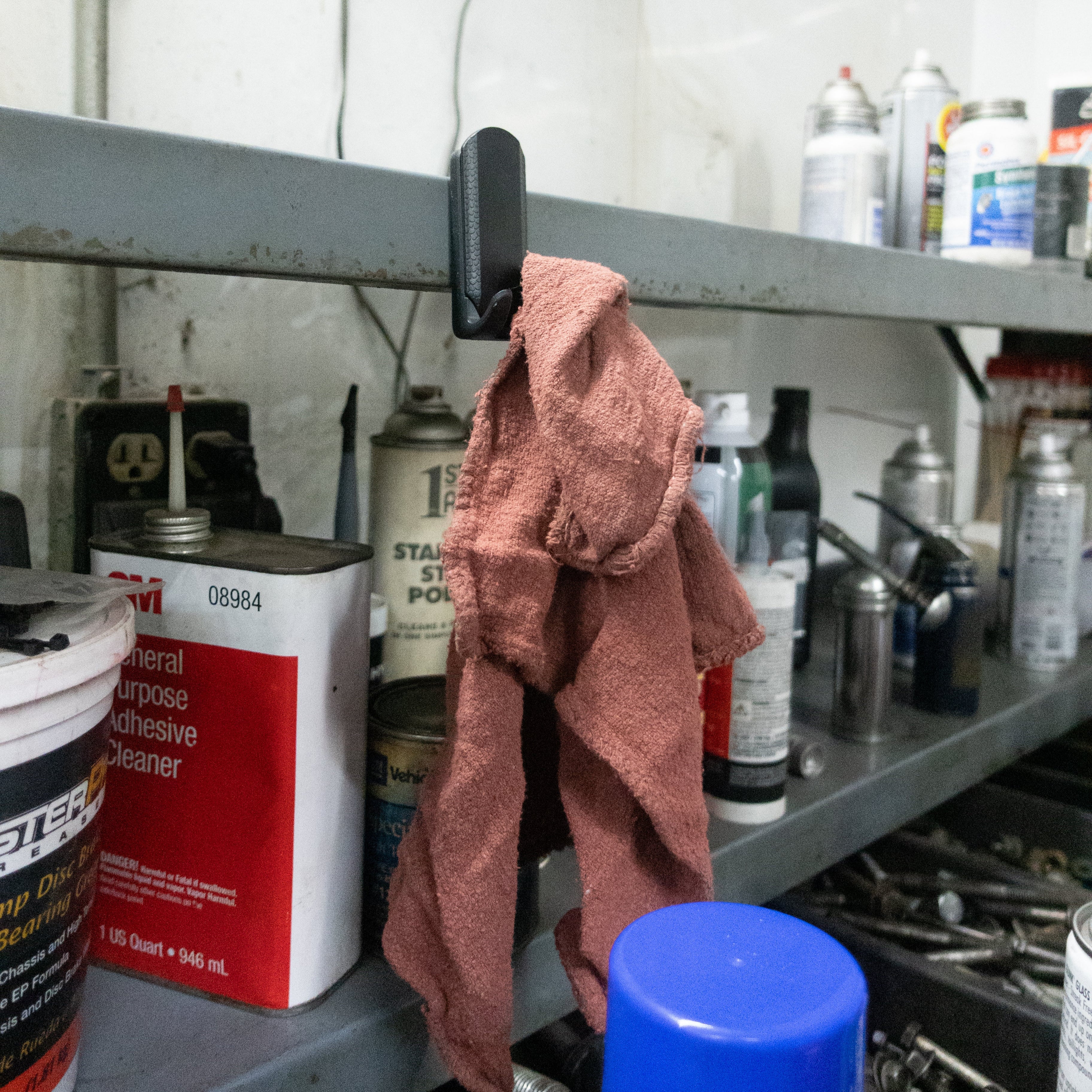 Black Gator magnetic hook holds a shop rag on a steel shelf beside spray cans and bottles.
