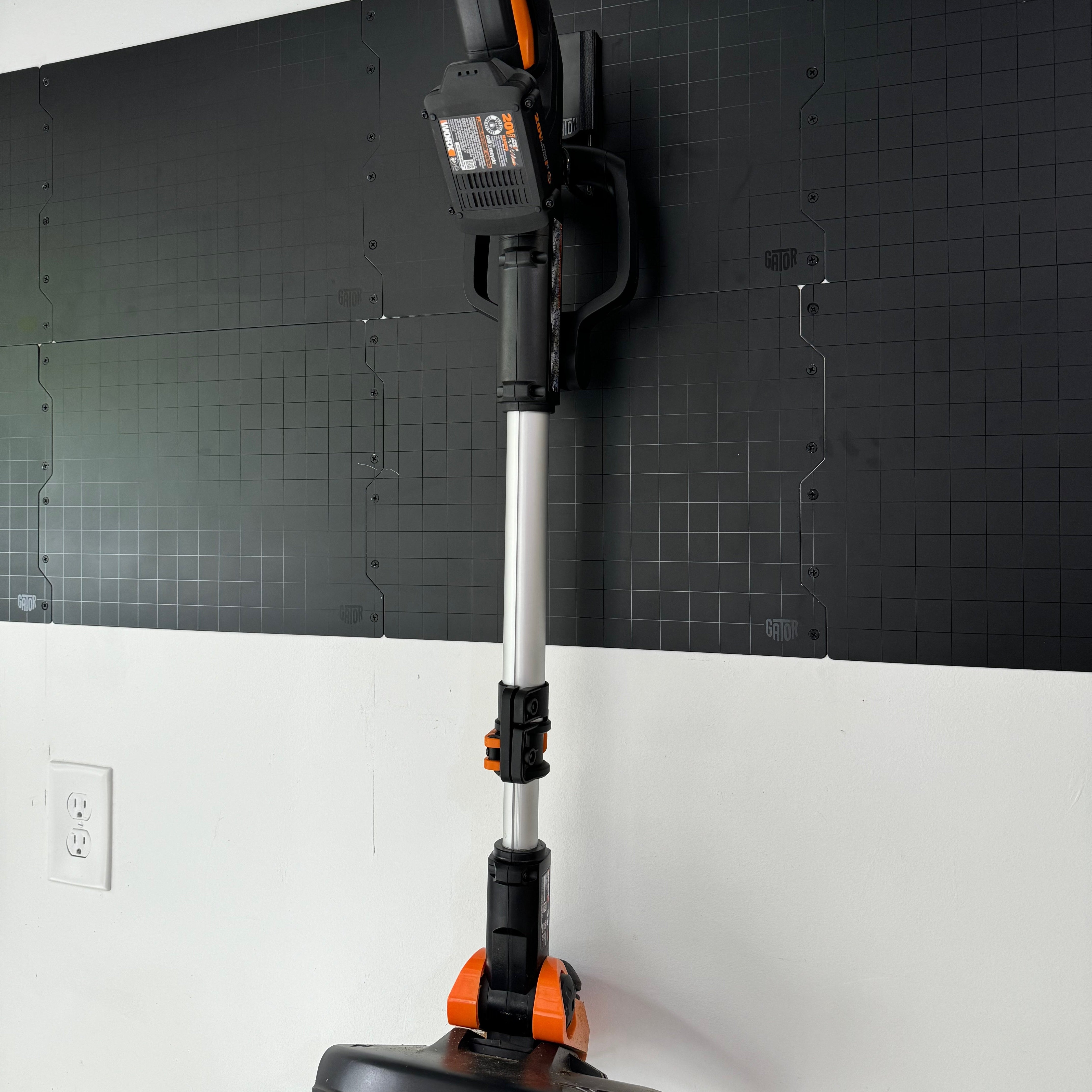 A cordless electric string trimmer is vertically hung on Gator Steel Wall Panels installed on a white painted wall.