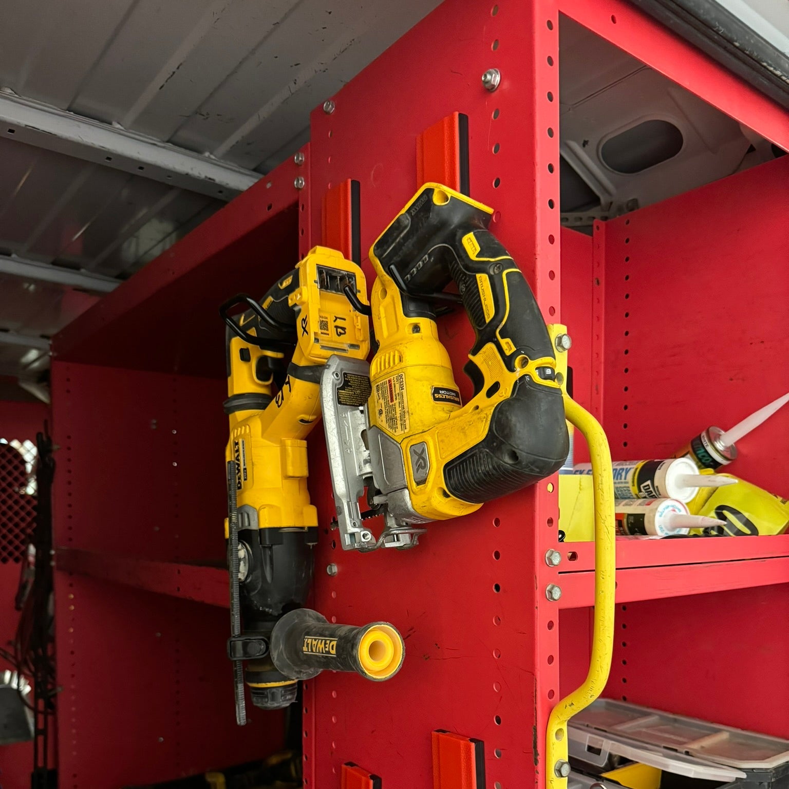 DEWALT jigsaw and reciprocating saw hanging from red Gator magnetic hooks on a red steel shelving unit.