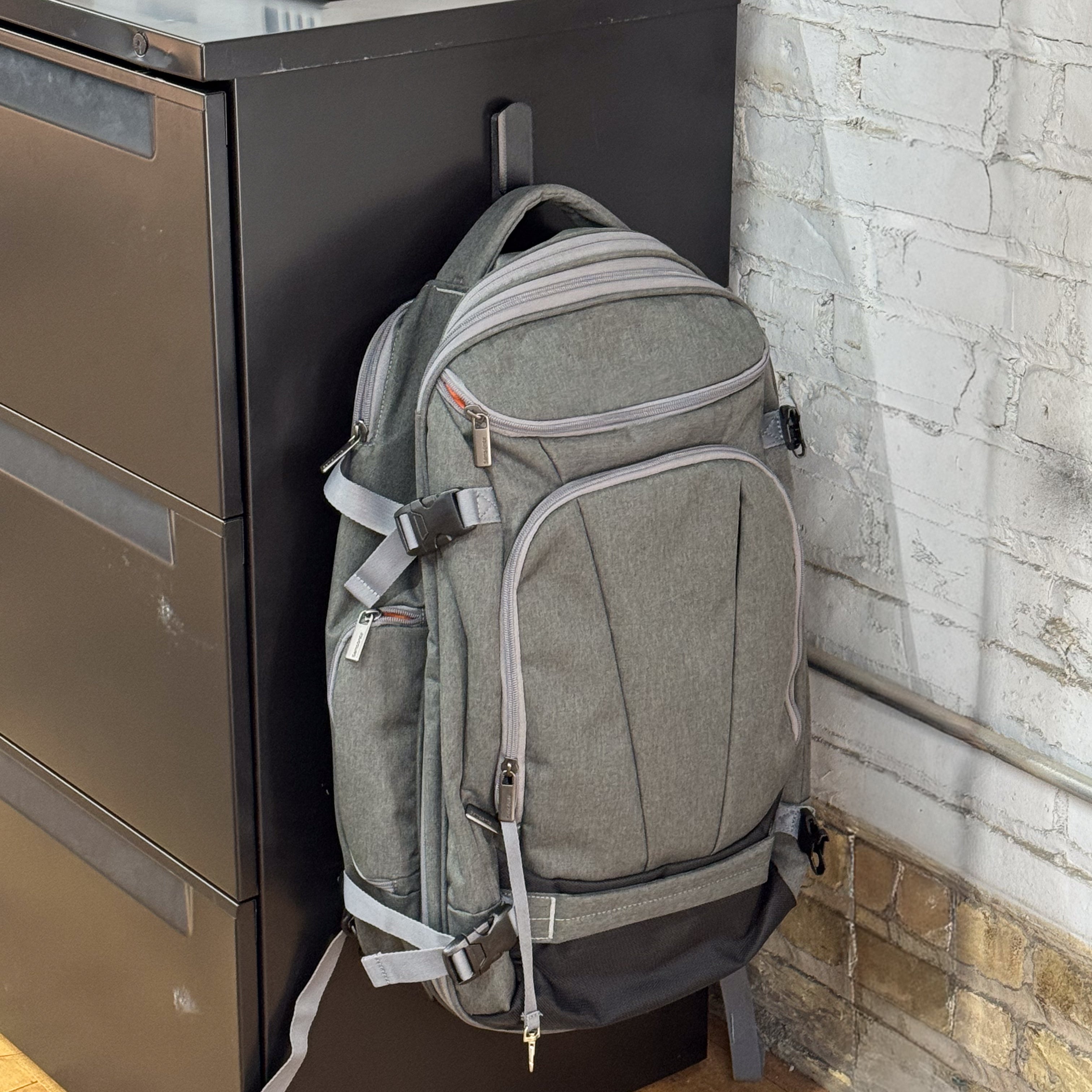 Gray backpack hanging from a red Gator magnetic hook on a black steel filing cabinet.