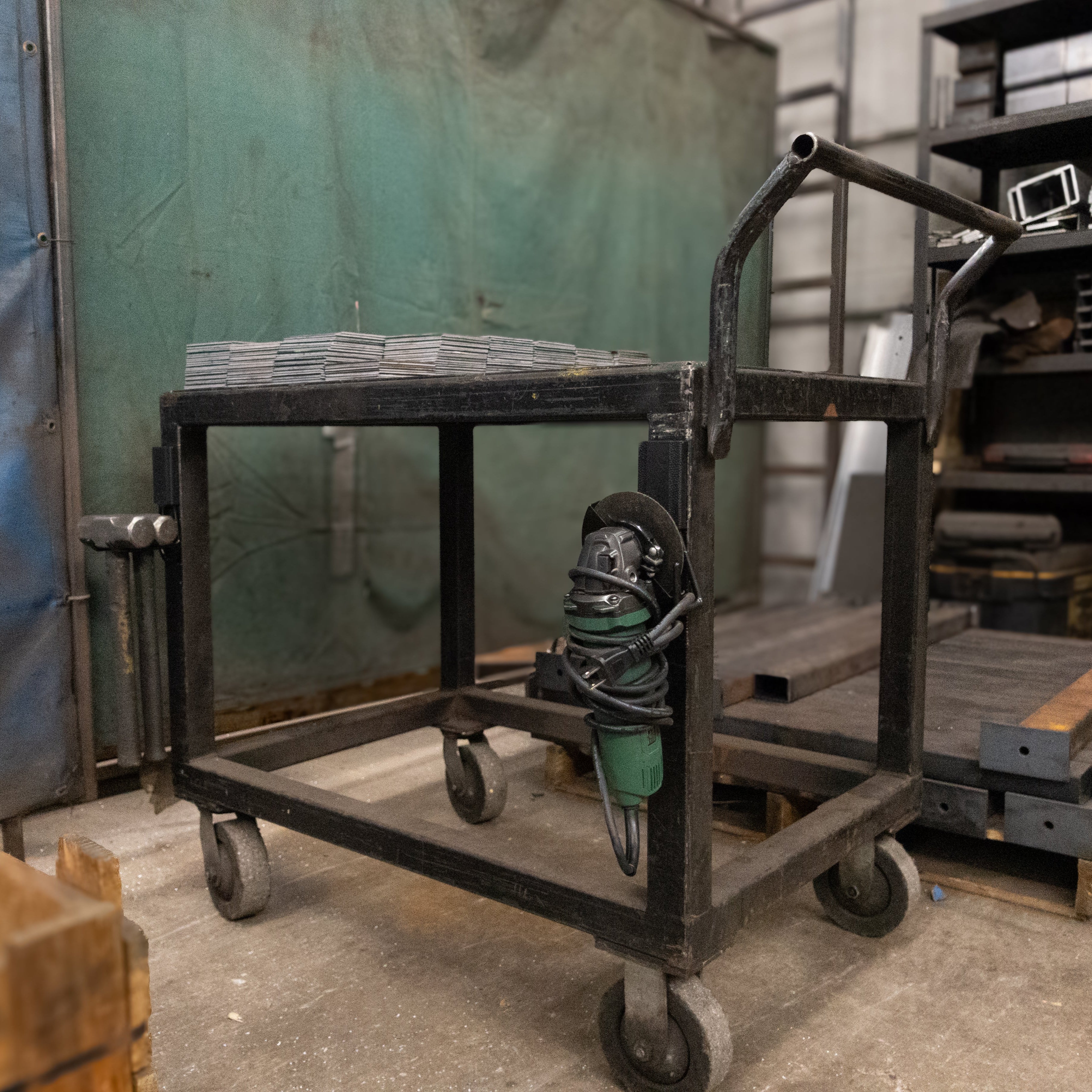 Green angle grinder hanging from a red Gator magnetic hook on a black steel shop cart.
