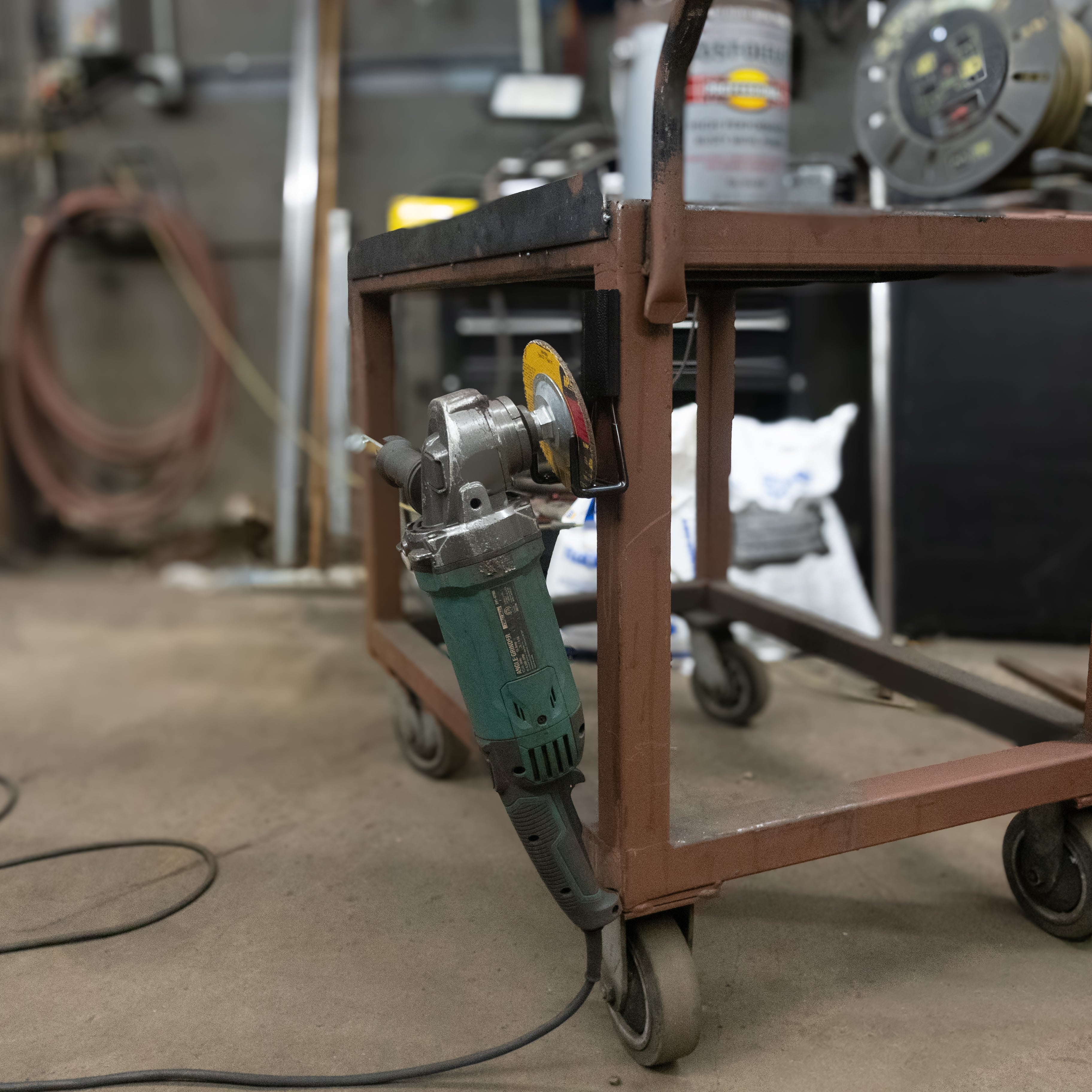 Green angle grinder hanging from a red Gator magnetic hook on a steel work cart.