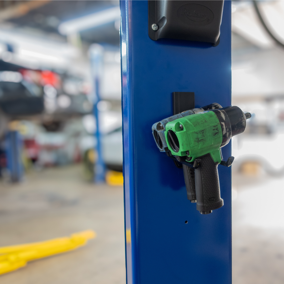 Gator Magnetics heavy duty magnetic hook holding two impact guns on steel beam in busy auto shop for secure tool storage and organization