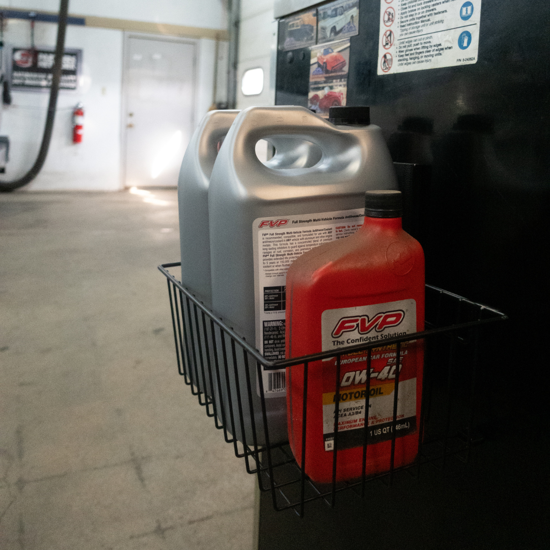 Gator Magnetics heavy-duty magnetic basket mounted on a steel tool box in an auto shop, holding FVP motor oil and coolant containers for convenient storage and organization of automotive fluids and supplies, with garage work area visible in the background.