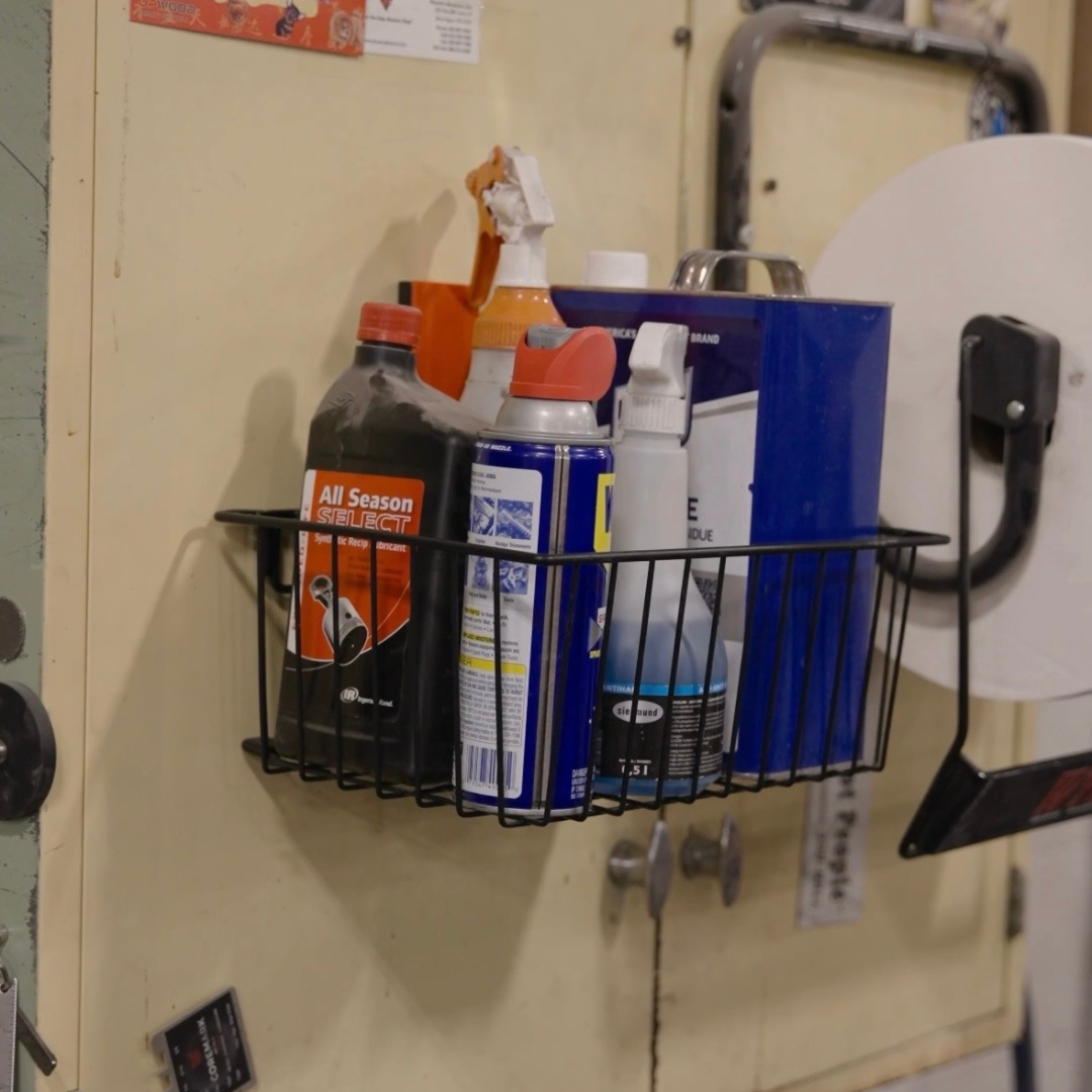 Gator Magnetics magnetic basket providing storage and organization on a metal tool cabinet in a workshop, holding lubricant, WD-40, spray bottles, and oil containers, keeping frequently used supplies off the workbench and within easy reach.