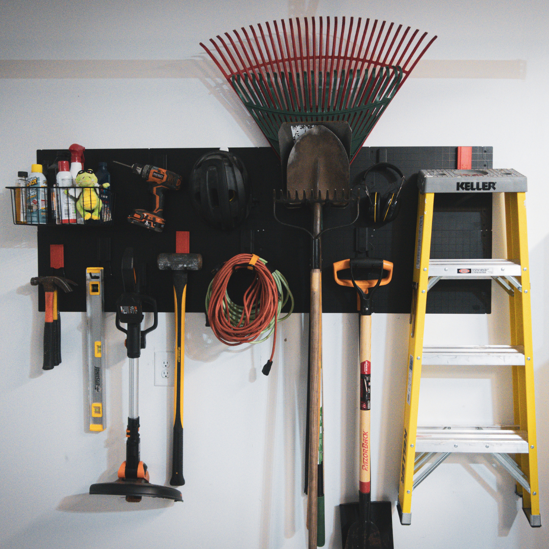Gator Magnetics magnetic hooks on a garage wall storage system holding a variety of tools including a rake, shovel, sledgehammer, extension cord, level, drill, and weed trimmer, alongside a yellow ladder and storage basket with cleaning supplies for efficient garage storage and organization.