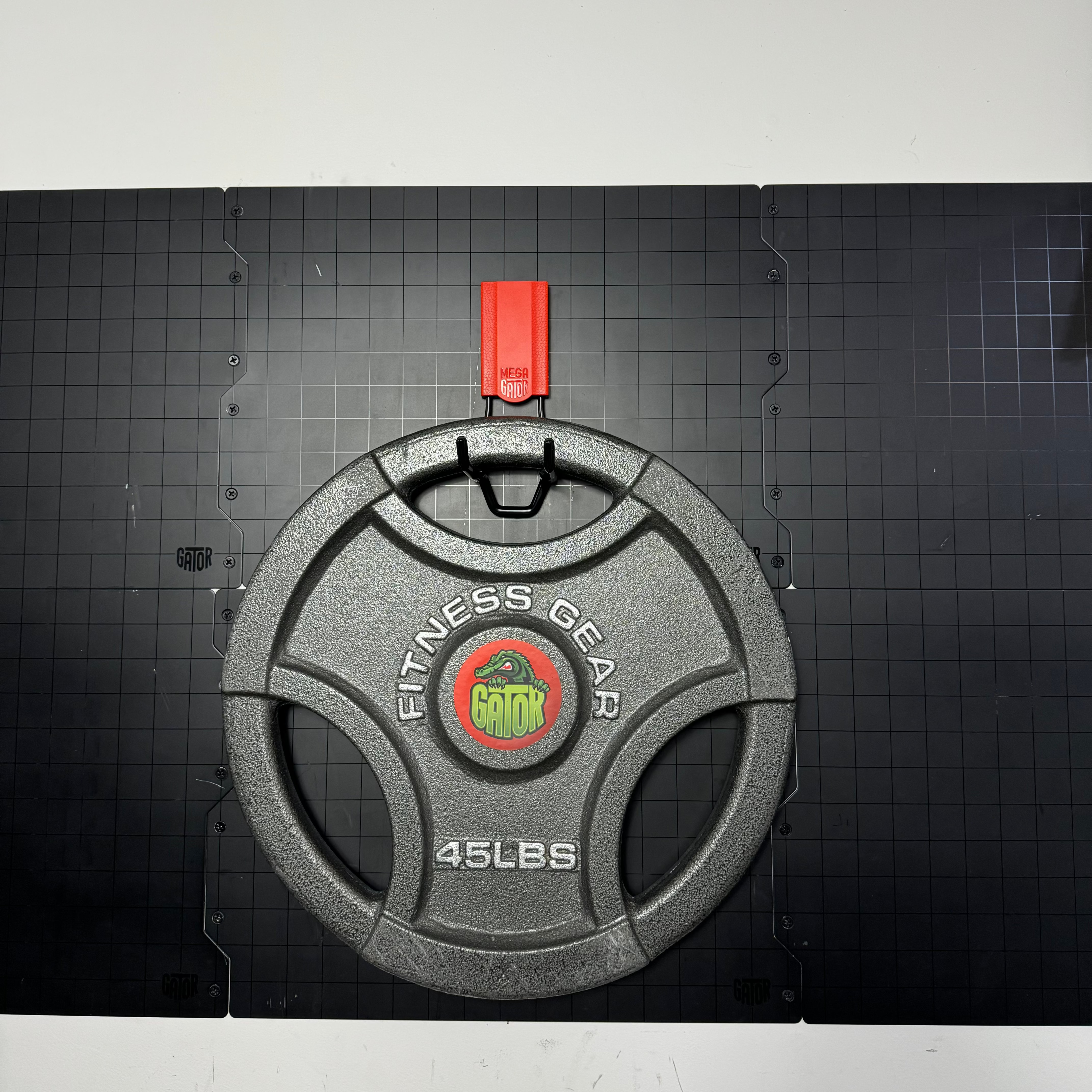 Gator Magnetics heavy-duty magnetic hook holding 45-pound Olympic weight plate on steel wall panel, demonstrating high load capacity.