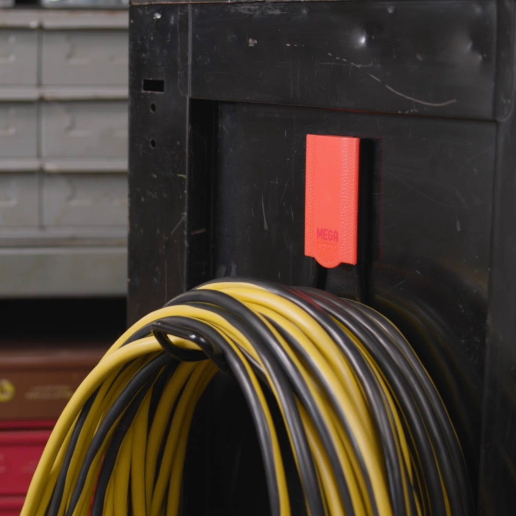 Gator Magnetics Mega magnetic hook holding a heavy-duty yellow and black extension cord on the side of a metal tool chest in a workshop, with storage drawers and toolboxes in the background for efficient workshop storage and organization.