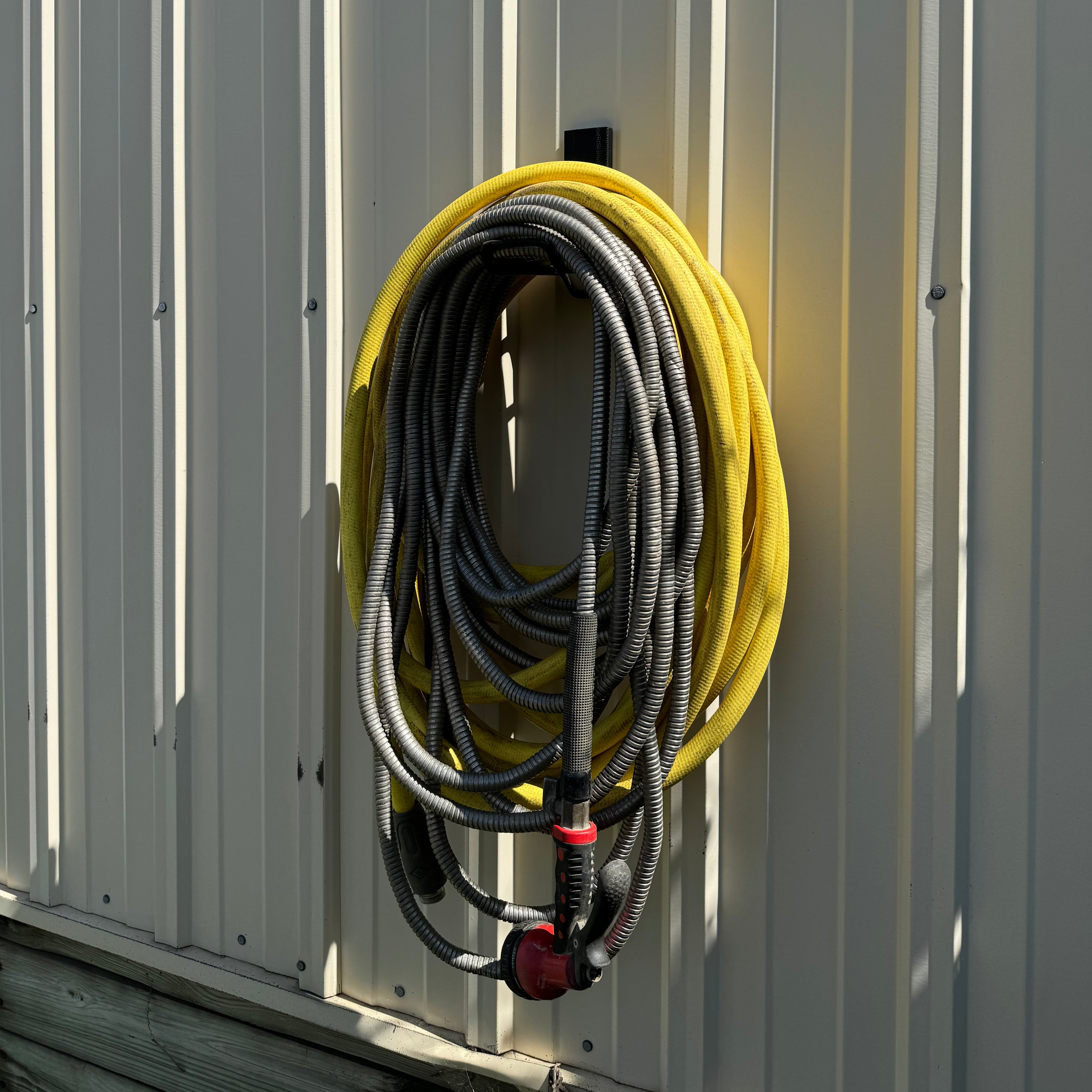 Red magnetic hook from Gator Magnetics secures coiled yellow and black hoses on a vertical steel wall panel outside.