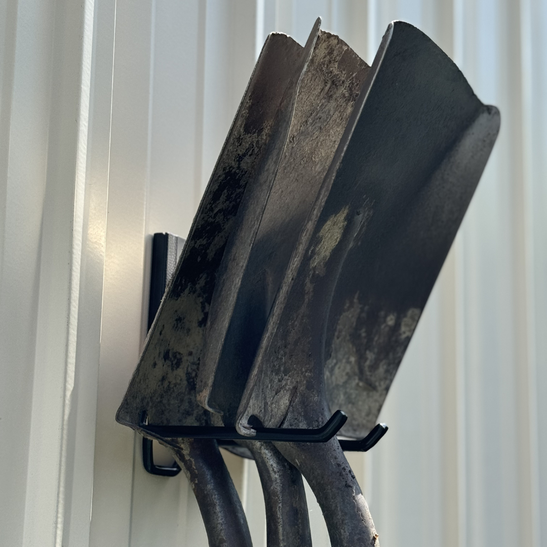 Three shovels hanging from a black Gator magnetic hook on a steel barn wall.