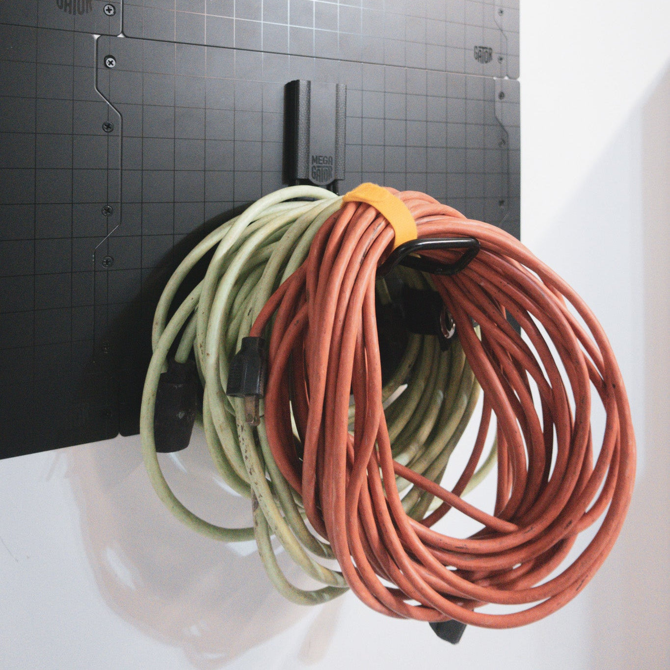 Two coiled extension cords, one green and one orange, are hung on a black Gator Magnetics hook attached to a steel wall panel.
