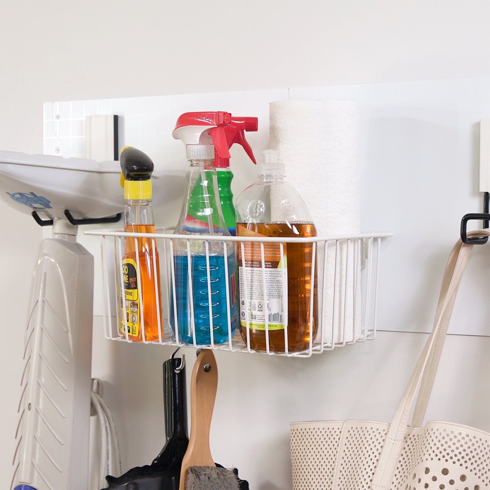 White Gator magnetic storage basket on a white steel wall panel holding spray bottles and soap.