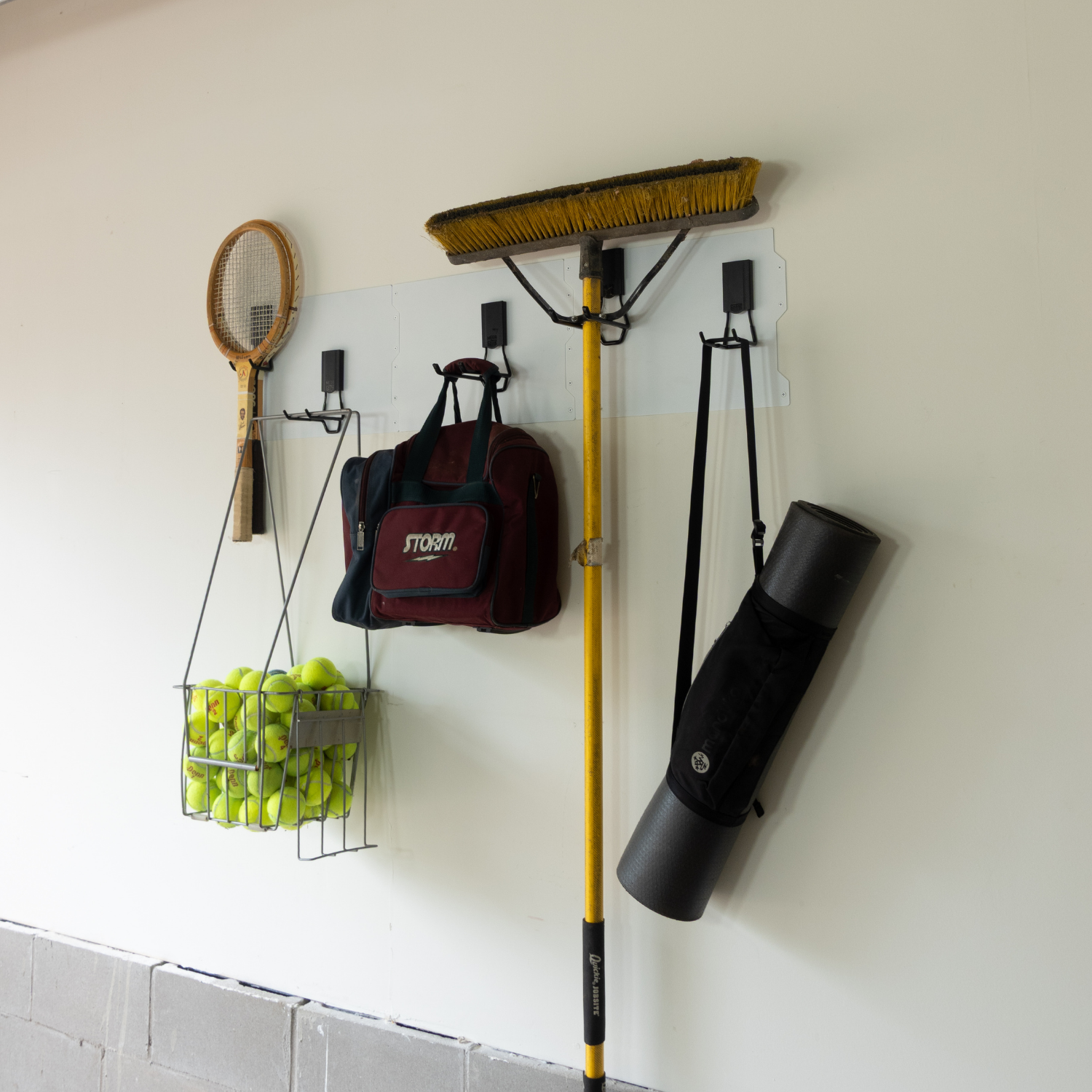White magnetic wall storage system holding a backpack, yard tools, tennis balls and a mat.