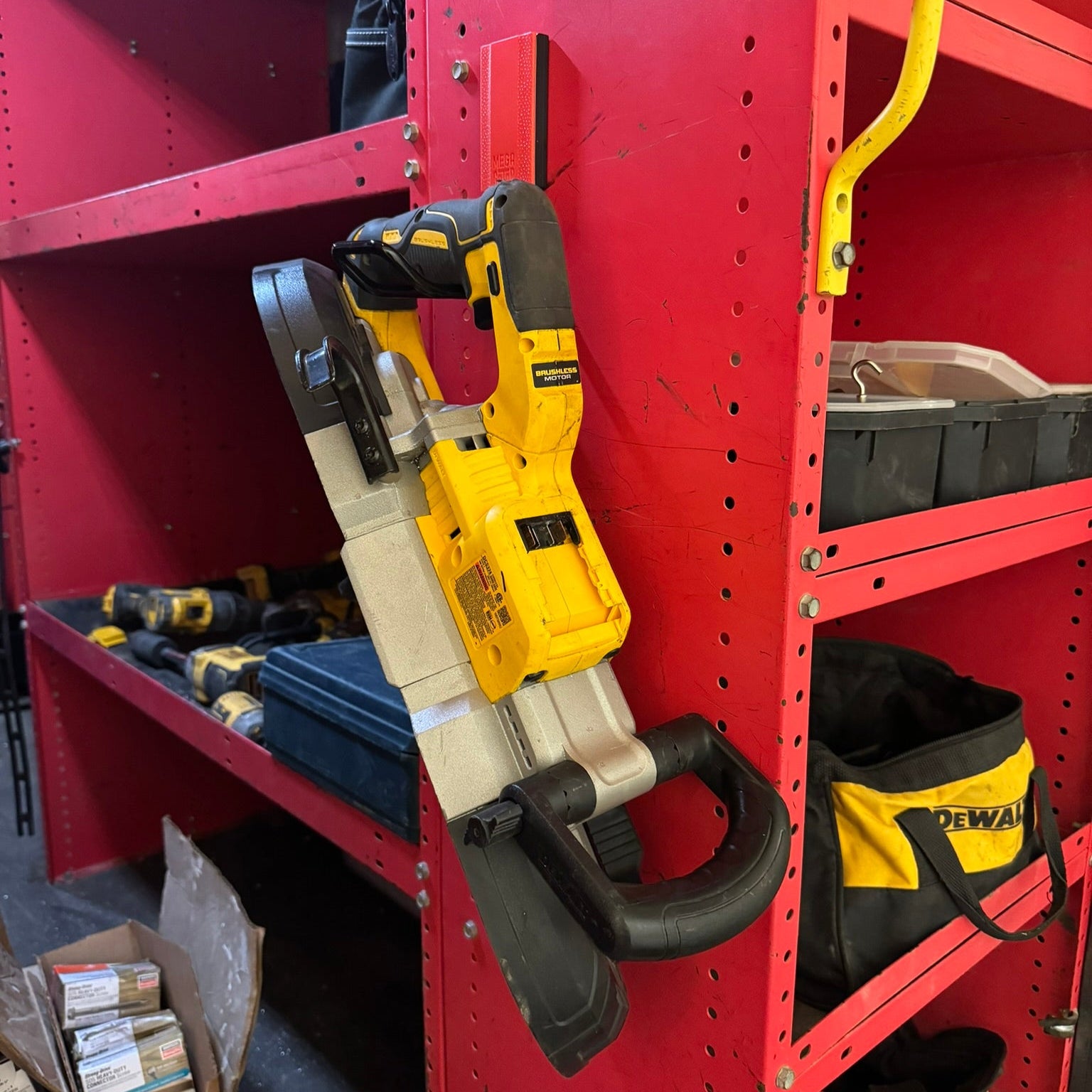 Yellow DEWALT band saw hanging from a red Gator magnetic hook on a steel shelving unit.