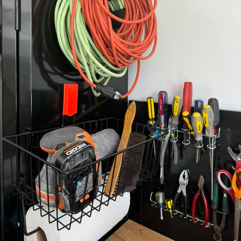 Magnetic basket mounted on a garage storage system and steel cabinet, holding a Ridgid power sander, cleaning brush, and paper towels, with an extension cord hanging above and screwdrivers, pliers, and scissors organized on a pegboard for efficient garage storage and organization.