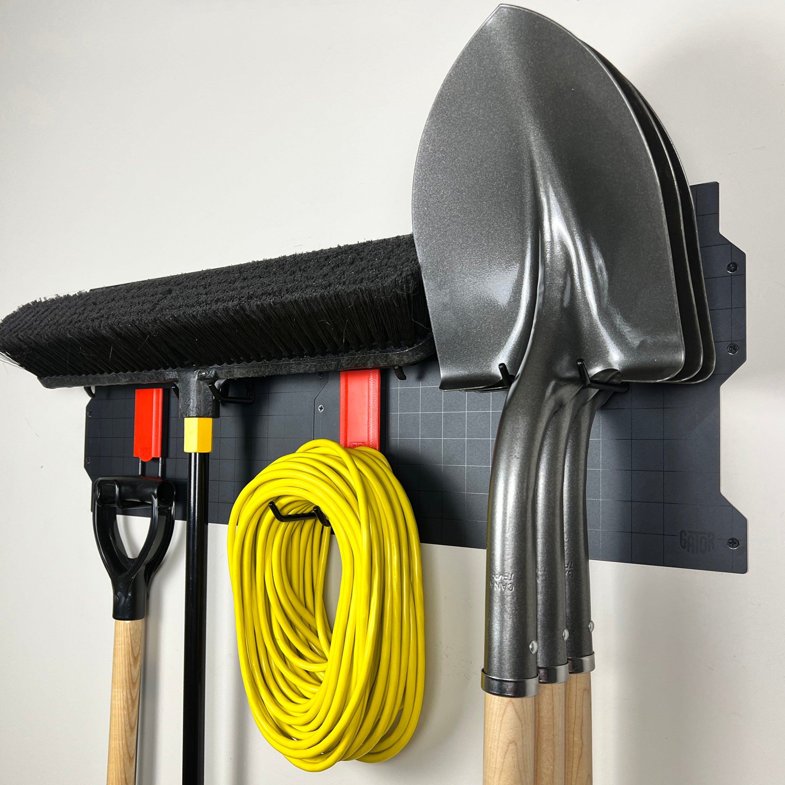 Magnetic hooks on wall panel holding brooms, shovel, and extension cord for organized garage or workshop storage.