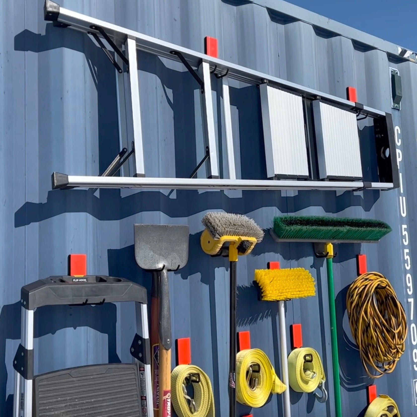 Heavy-duty magnetic hooks organizing ladders, brooms, shovels, tow straps, and extension cords on a shipping container wall for secure outdoor tool storage.