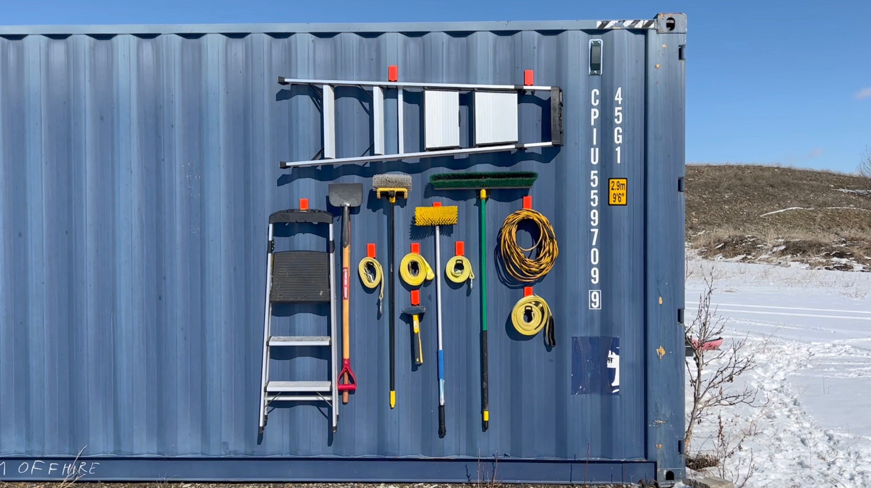 Magnetic hooks being used on a steel shipping container to hold heavy equipment like ladders, extension cords and more, providing a storage solution that doesn't require drilling holes in the shipping container steel walls.