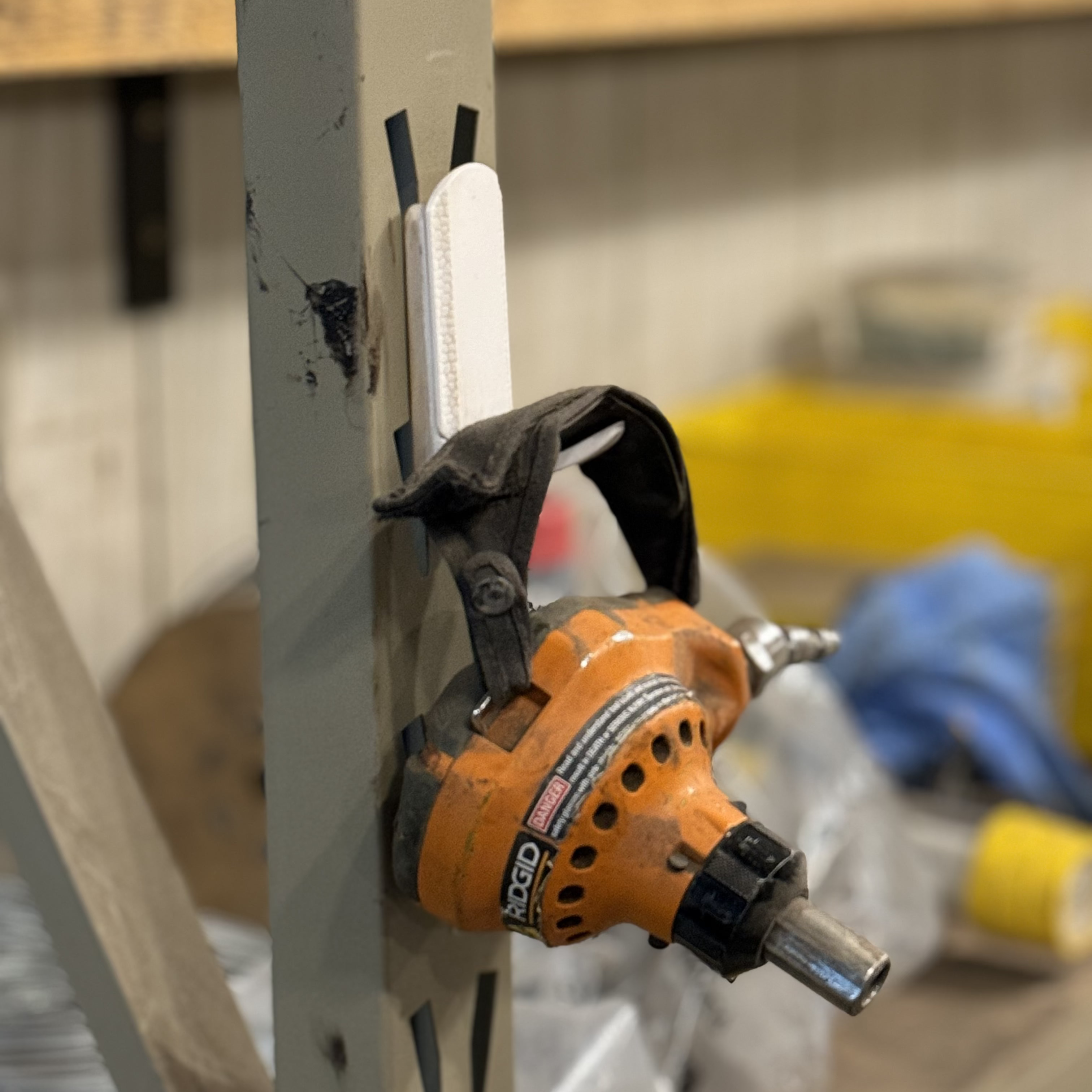 White magnetic hook attached to a steel post holding an orange pneumatic tool, showcasing heavy-duty industrial equipment organization.