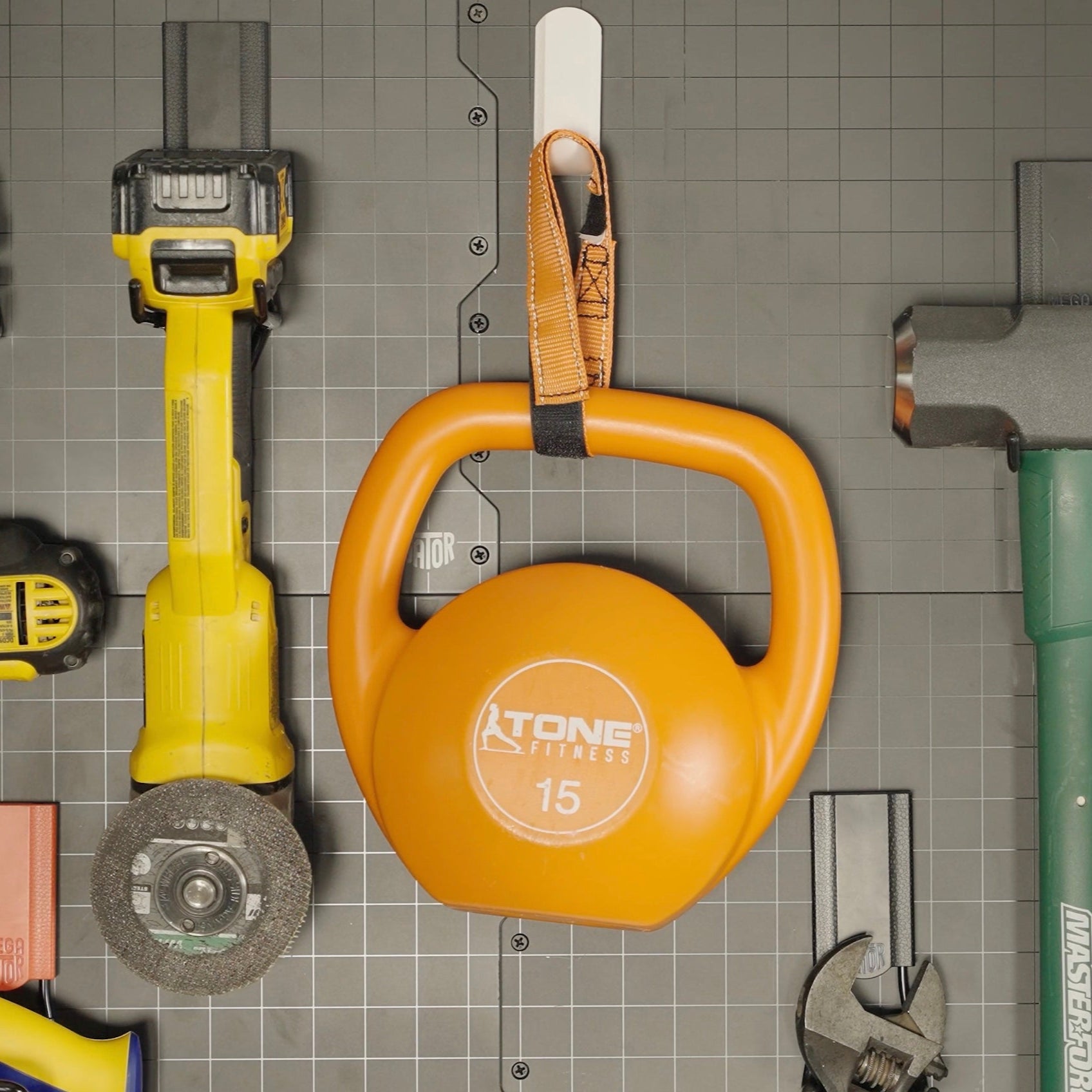 White magnetic hook mounted on a steel wall panel holding a 15-pound orange kettlebell with tools organized around it, showcasing heavy-duty storage strength and versatility.