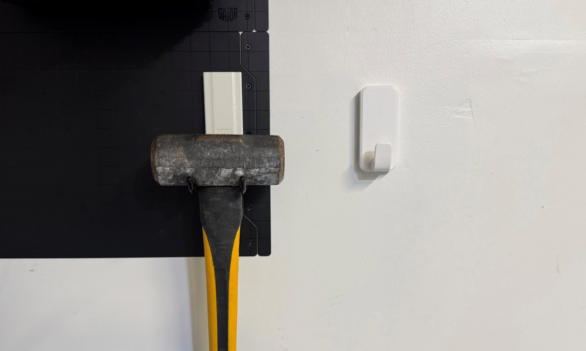 Sledgehammer on a red Gator magnetic hook beside a white adhesive hook comparison.