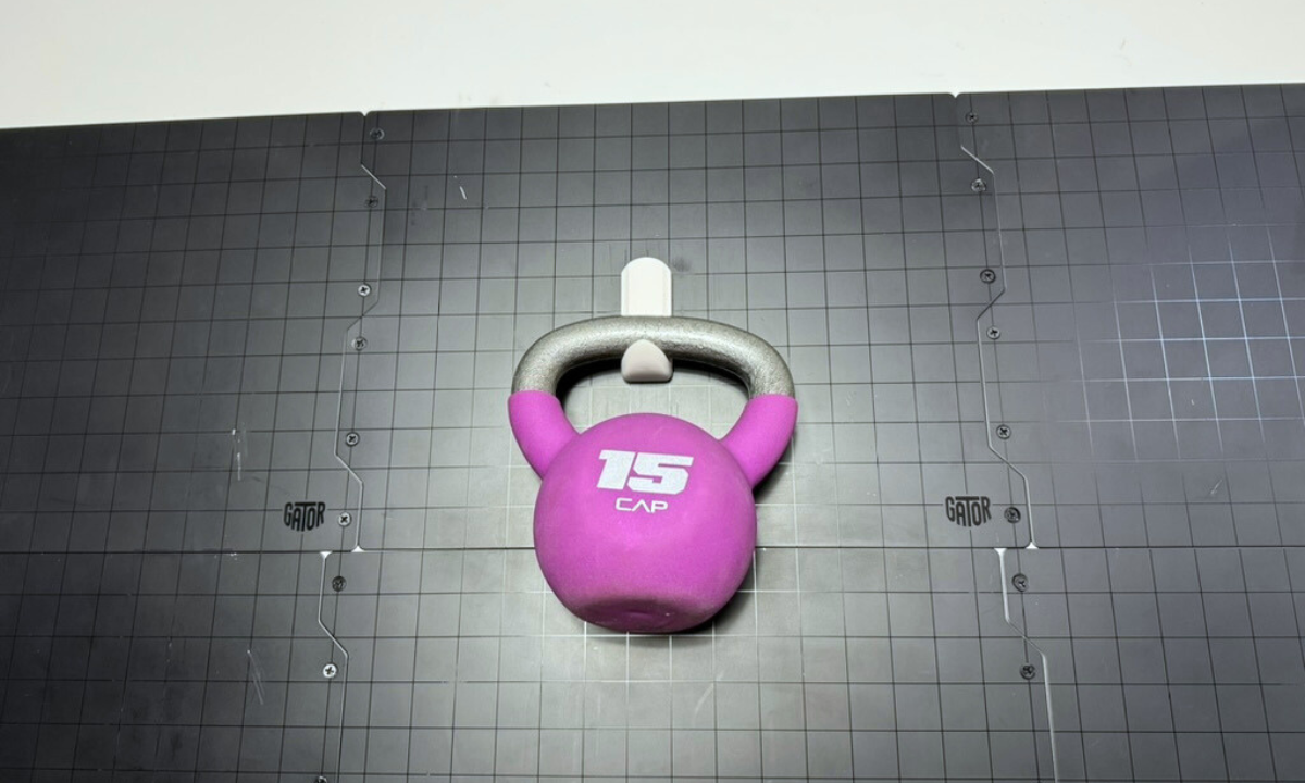 Purple 15-pound kettlebell on a black steel wall panel surrounded by small adhesive hooks.
