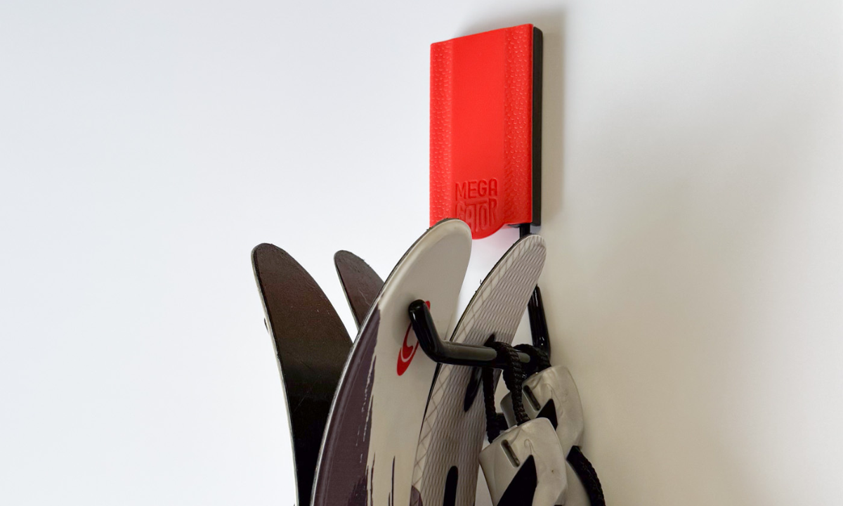 A Gator Magnetics red magnetic hook hangs a pair of black and white skis from a steel wall panel.