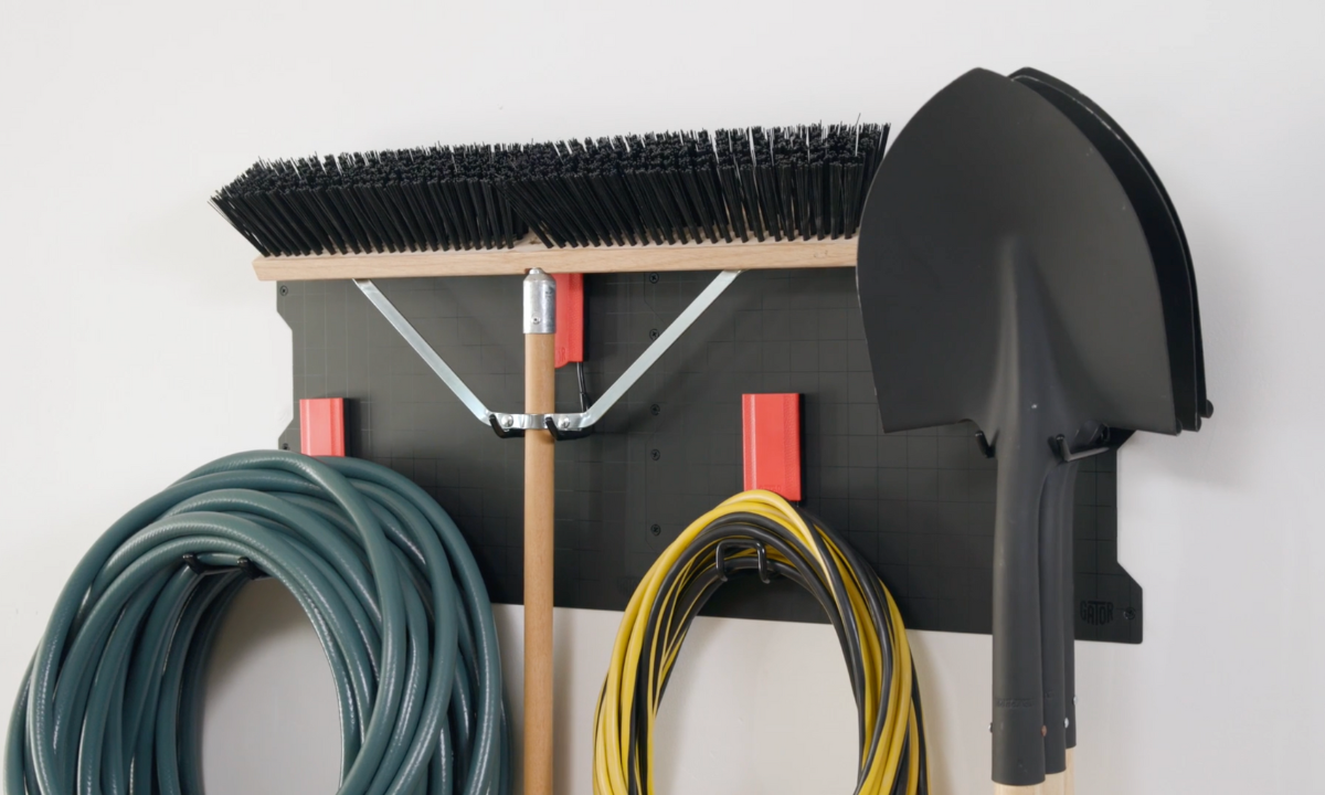 Gator Steel Wall Panel holding a garden broom, bristle brush and coiled hose with red magnetic hooks.