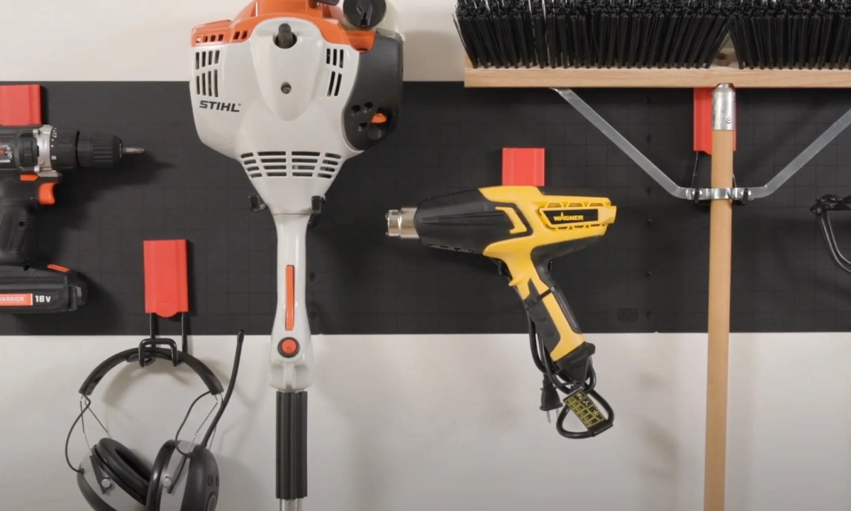 Black Gator Steel Wall Panel with red magnetic hooks holding a drill, trimmer, heat gun, headset and broom.