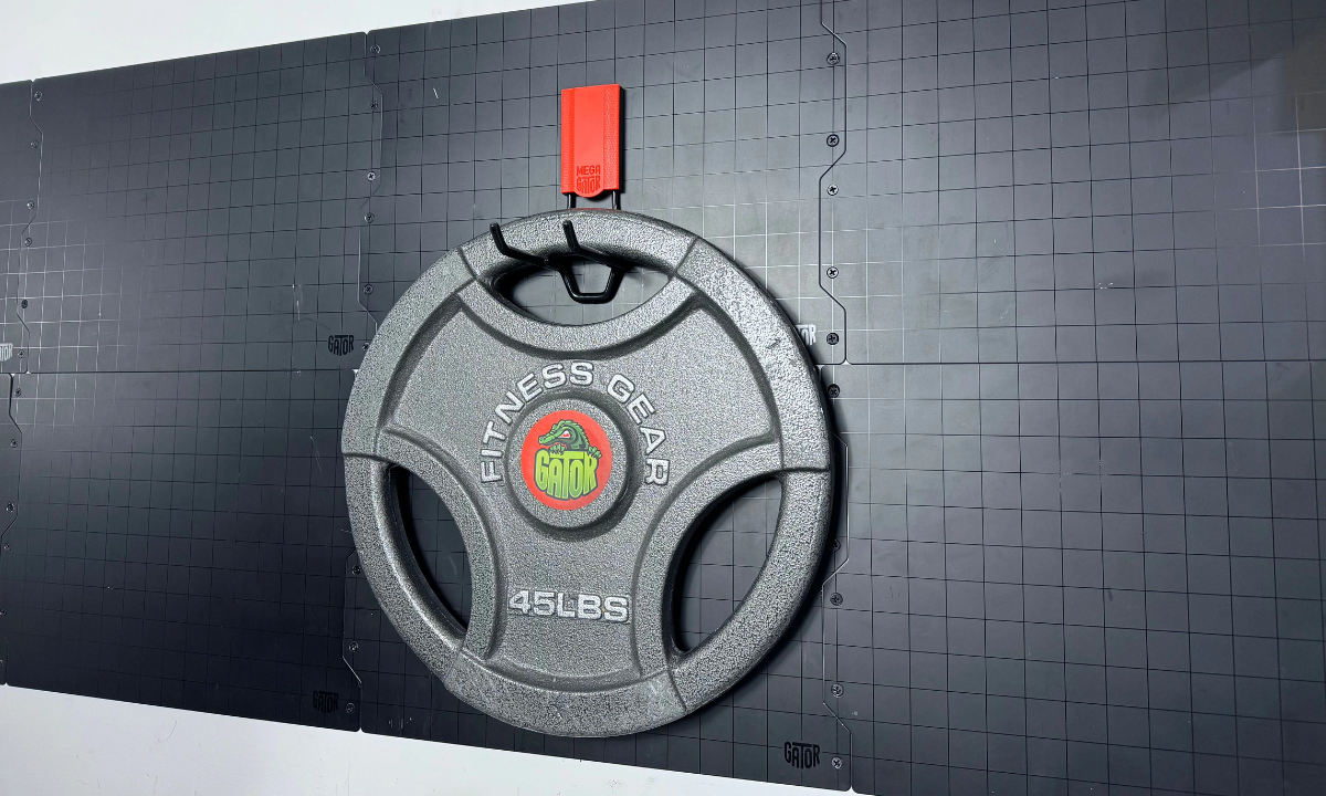 Black 45-pound weight plate hanging from a red Gator magnetic hook on a black steel wall panel.