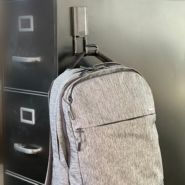 Black 2.5" closed magnetic hook holding a black backpack, with a 25 lbs capacity. Ideal for organizing backpacks, tools, and other items in home garages, workshops, and industrial spaces. Provides strong magnetic attachment and a sleek design for efficient storage.
