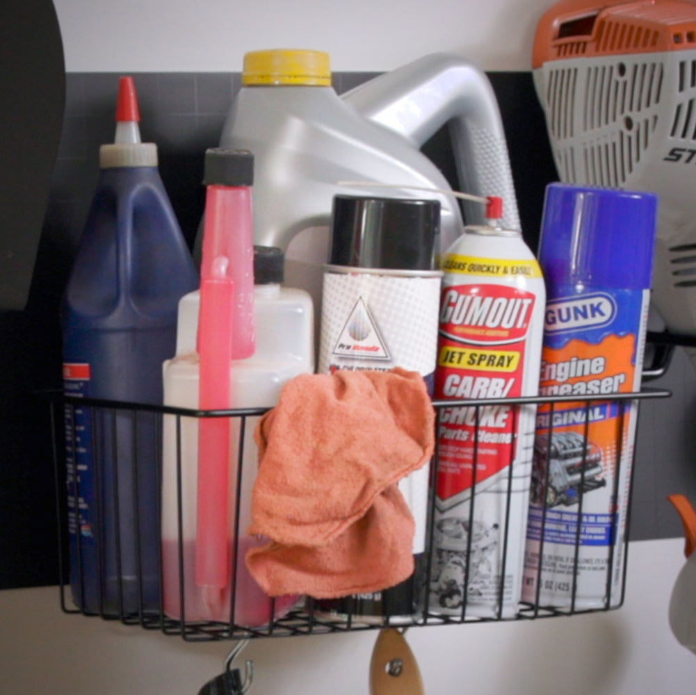 The 12" Small Utility Basket with a black lever is shown holding various car servicing products, including jet spray, engine grease, and oil. This basket provides a convenient and secure storage solution for automotive essentials, while its magnetic hold ensures stability on steel surfaces. In the background, a 4" Open Hook holds a weed wacker, and another hook supports a shovel.