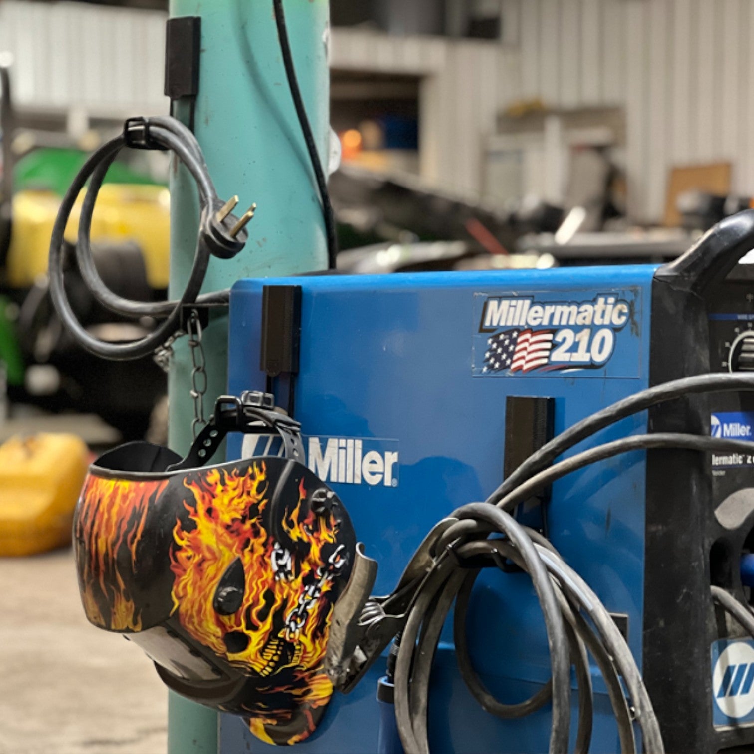 Heavy-duty magnetic hooks providing welding storage and organization for a flame-painted welding helmet and welding cables on a MillerMatic 210 welder and gas cylinder. Perfect for keeping gear secure and accessible in workshops, garages, and fabrication shops.