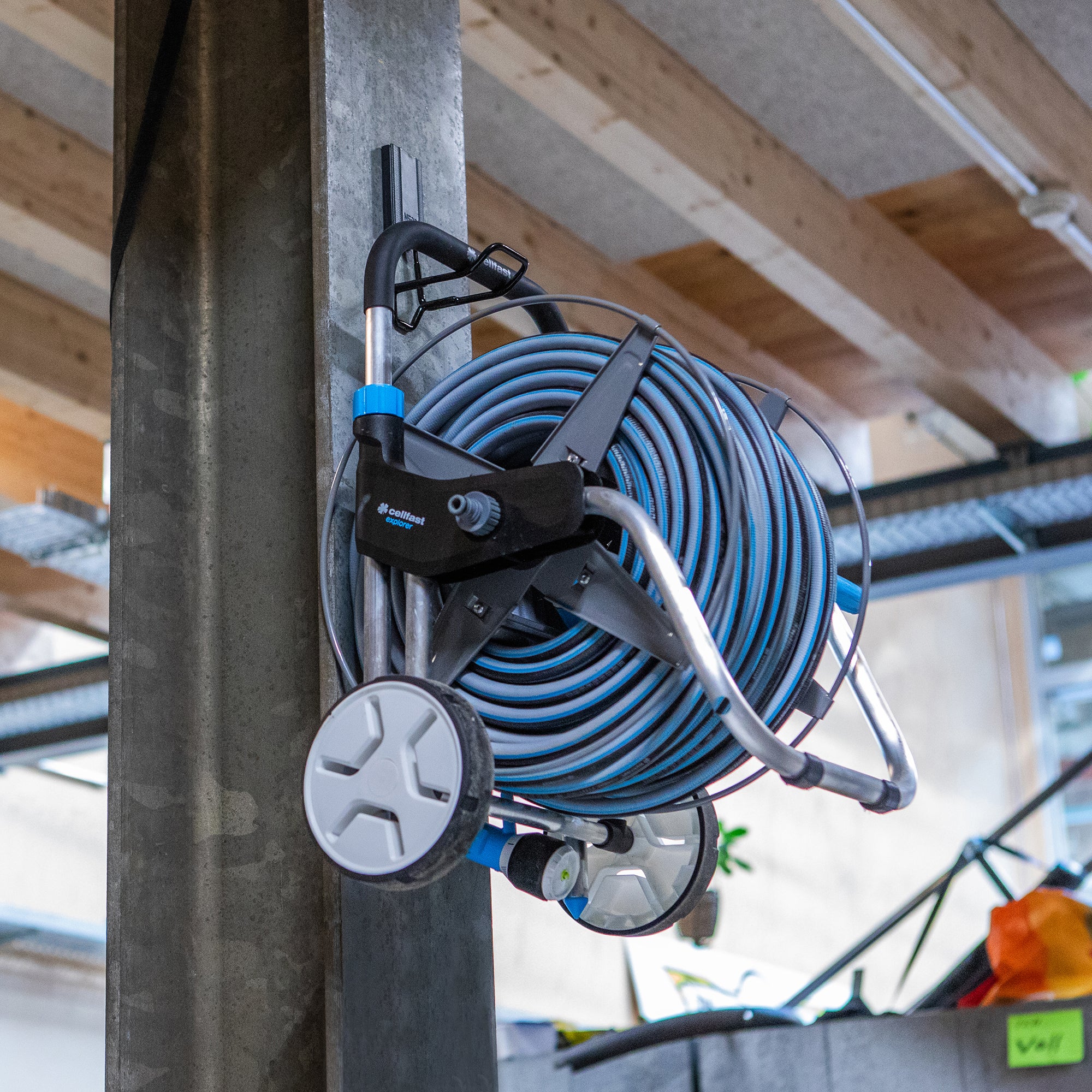 Gator Magnetics 4.5 inch closed magnetic hook holding blue garden hose reel with wheels on steel beam in workshop, heavy-duty magnetic hook for garden hose, garage storage magnetic hook, Gator Magnetics magnetic hook for hose management, industrial magnetic hook for shop equipment.
