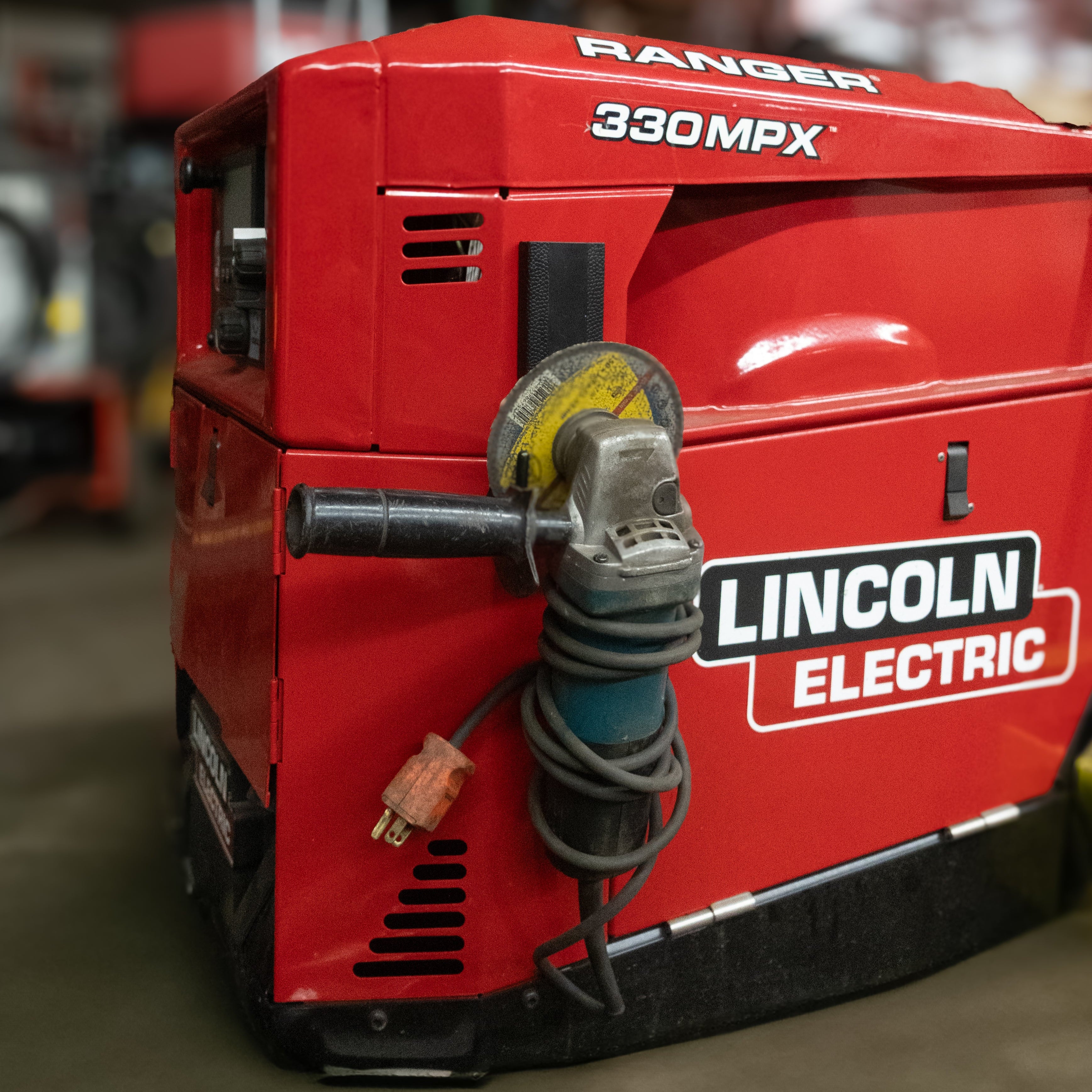 Angle grinder with coiled cord hanging from a red Gator magnetic hook on a Lincoln Electric welder.