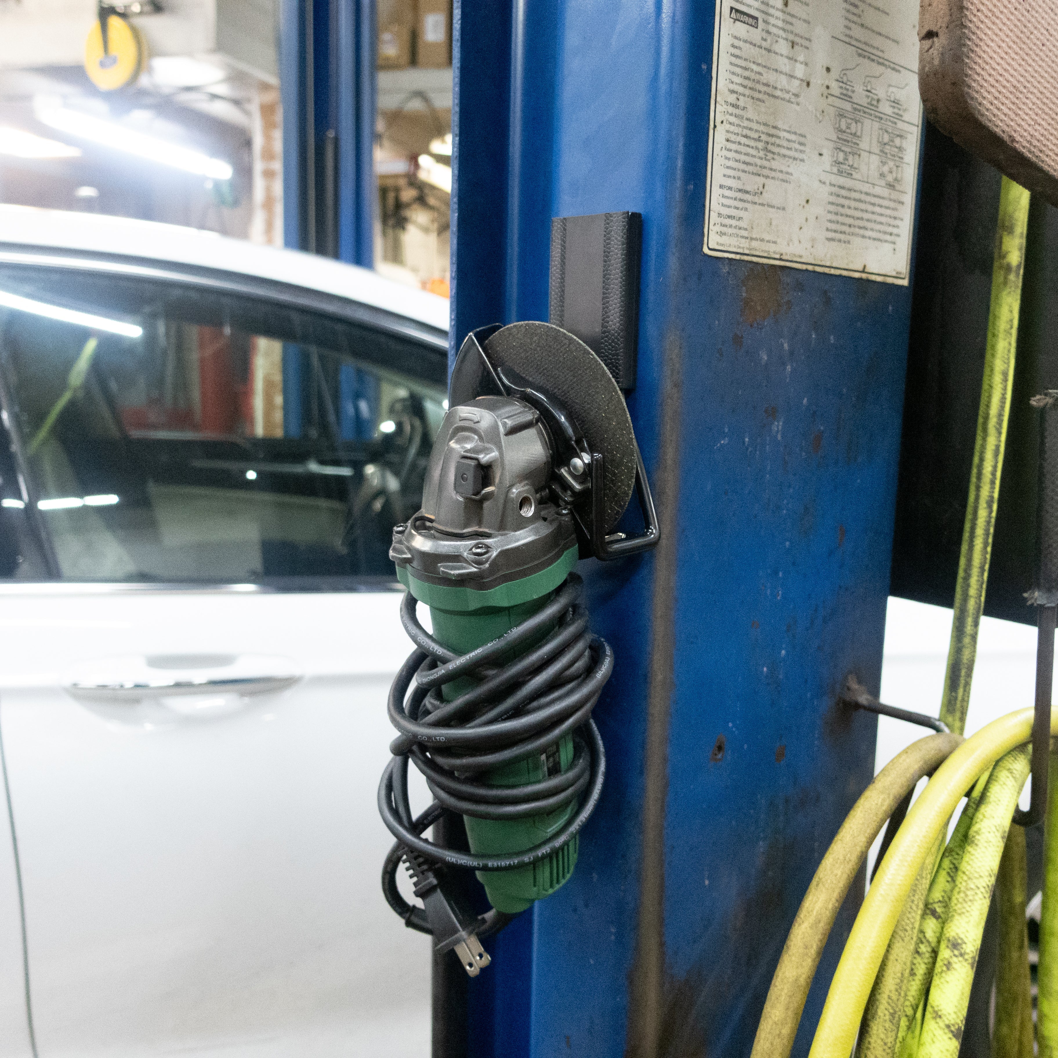 Angle grinder with wrapped cord hanging from a black Gator magnetic hook on a blue steel post.