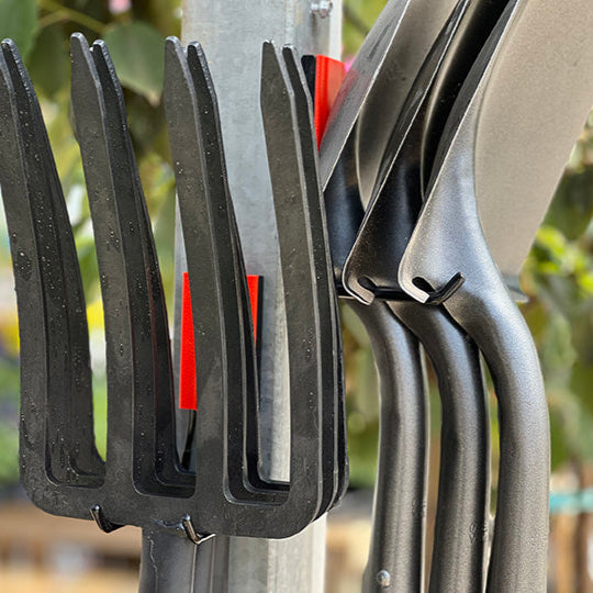 Black garden rakes are hung on a vertical steel pole using red Gator Magnetics magnetic hooks in an outdoor setting.